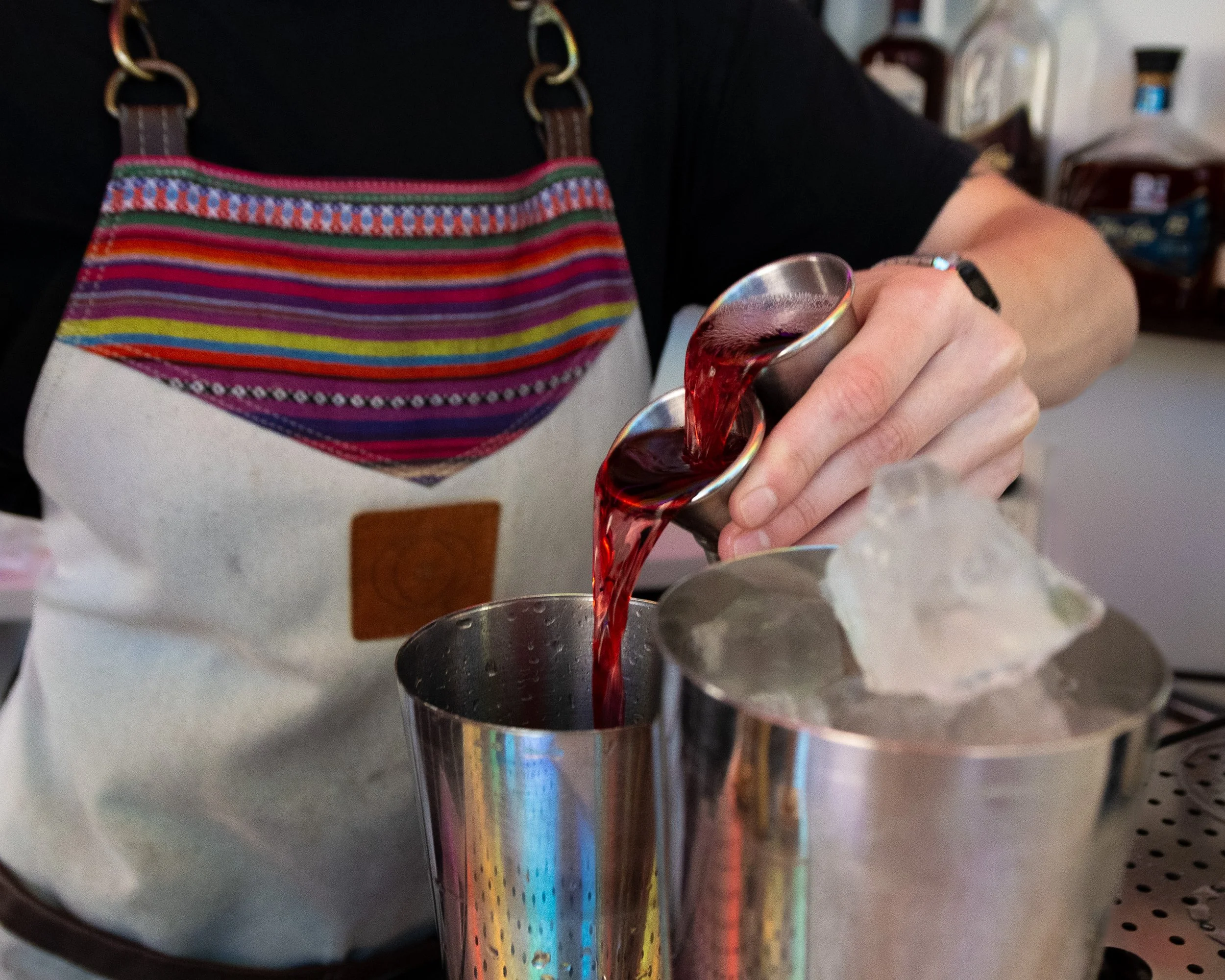 Person pouring red liquid into a metal container while wearing a colorful striped apron.
