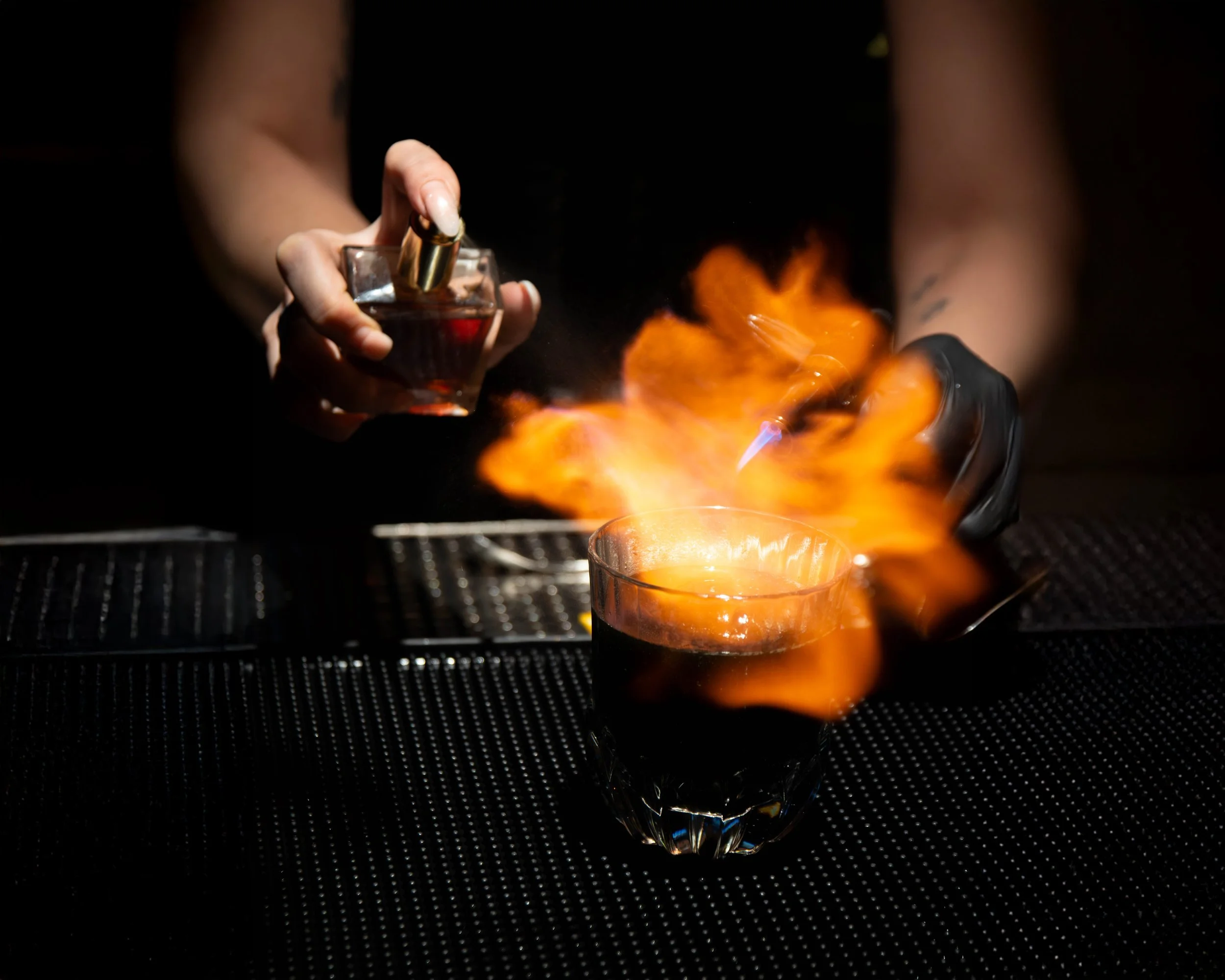 Person holding a perfume bottle near a glass with flames.