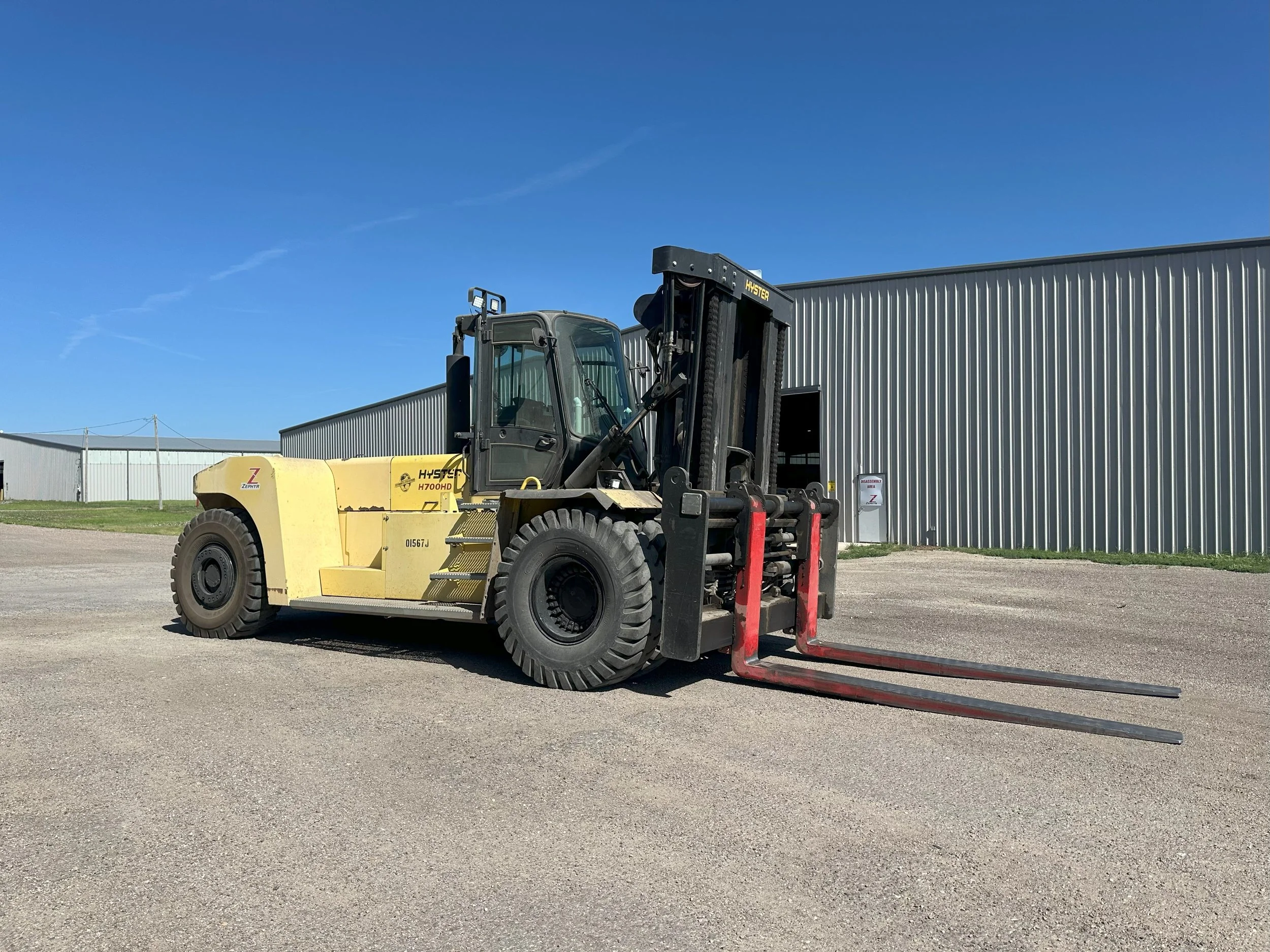 Yellow forklift truck parked on gravel ground outside near a large metal building under a clear blue sky.