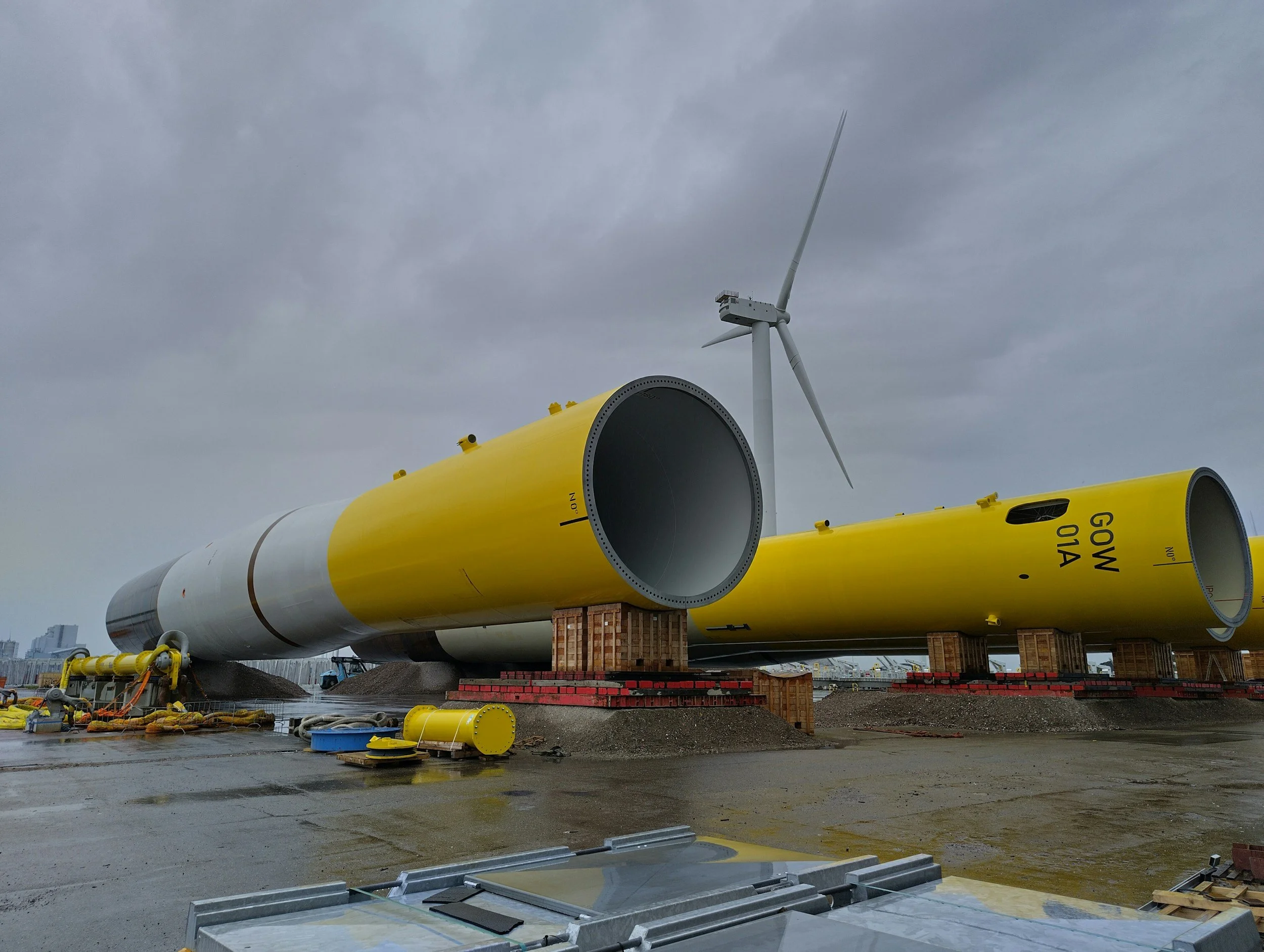 Large industrial wind turbine blades under construction, with gray cloudy sky in the background, at a construction site.