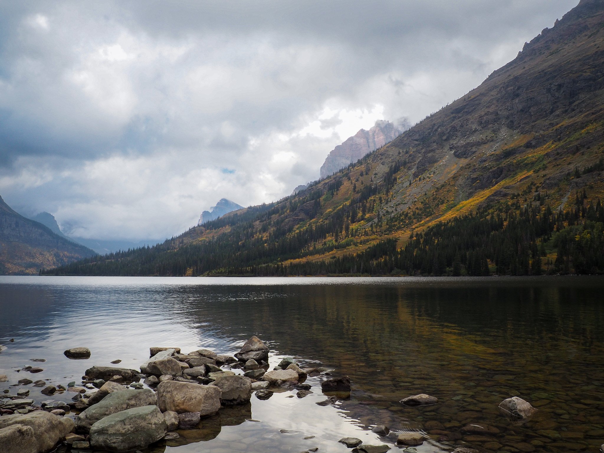 A serene early morning at Two Medicine Lake in Glacier National Park, Montana. The water is calm with the scenery softly reflecting on the surface of the water.