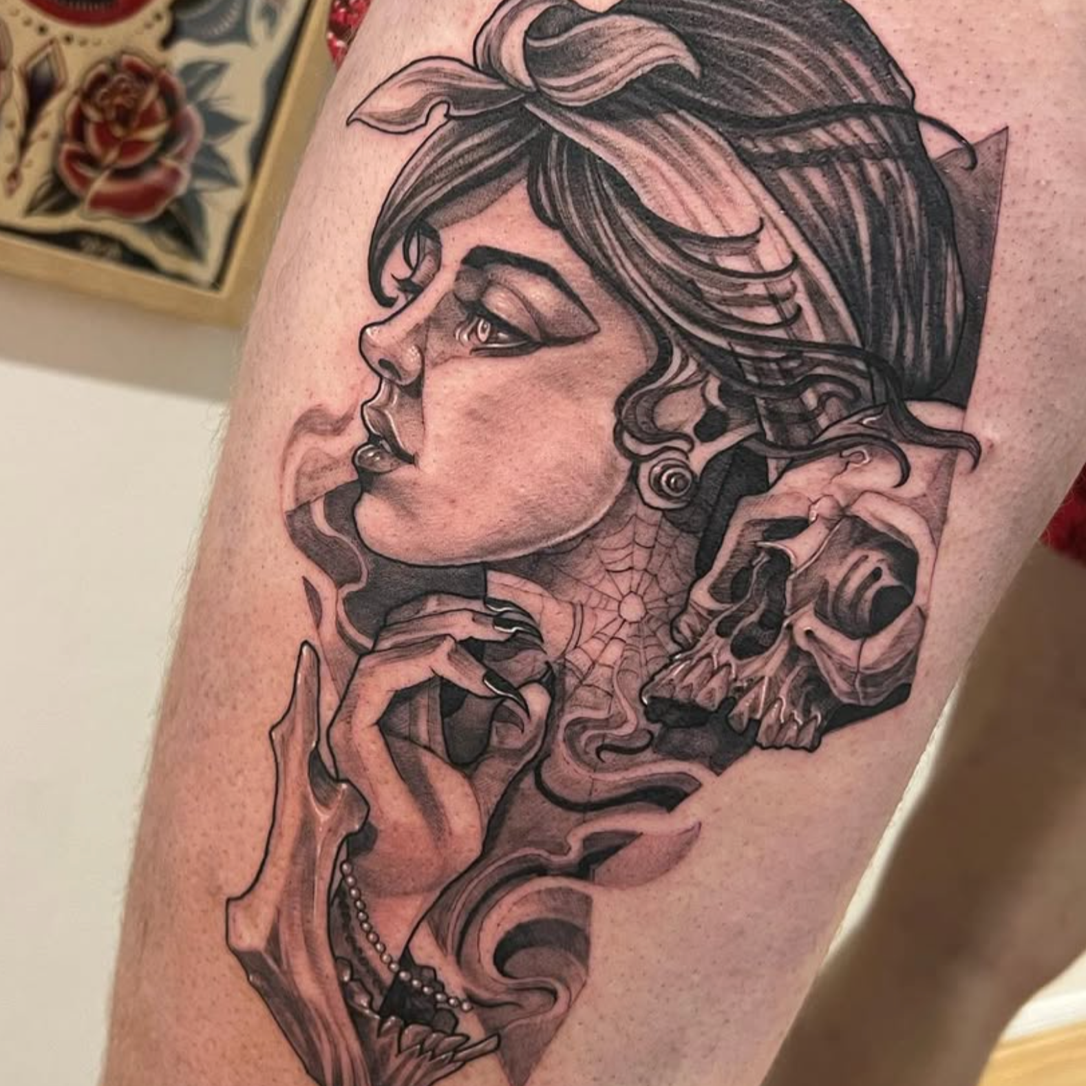 Tattoo of a woman's profile with hair, skull, spiderweb, pearls, and floral details.