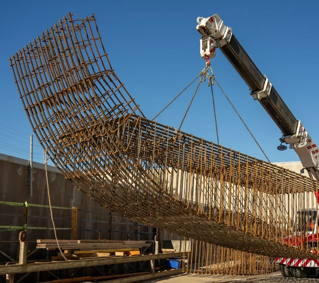 Crane lifting large prefabricated steel reinforcement cage at Carrabay fabrication yard.