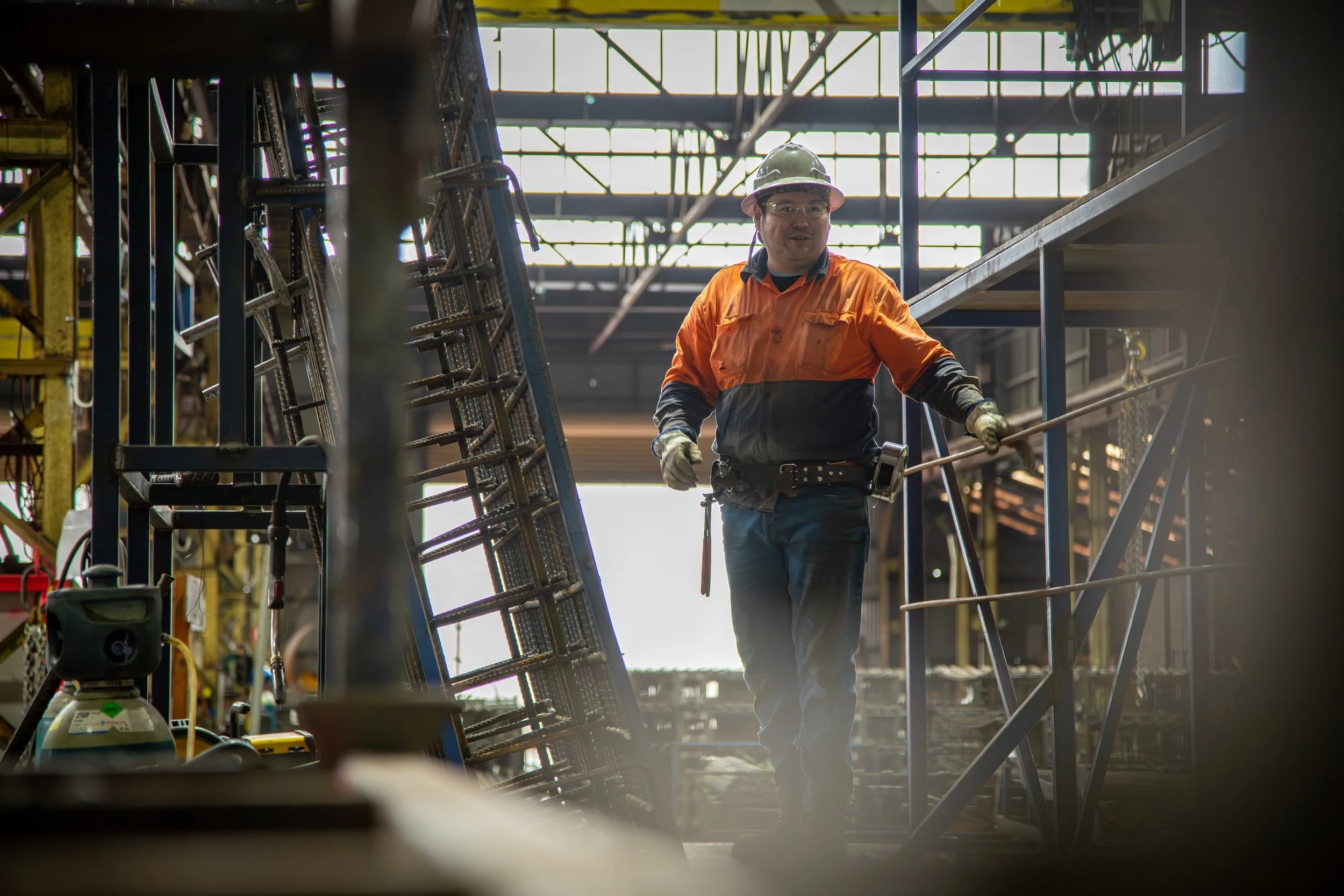 Worker in PPE and tool belt managing reinforcement steel assembly at Carrabay facility.