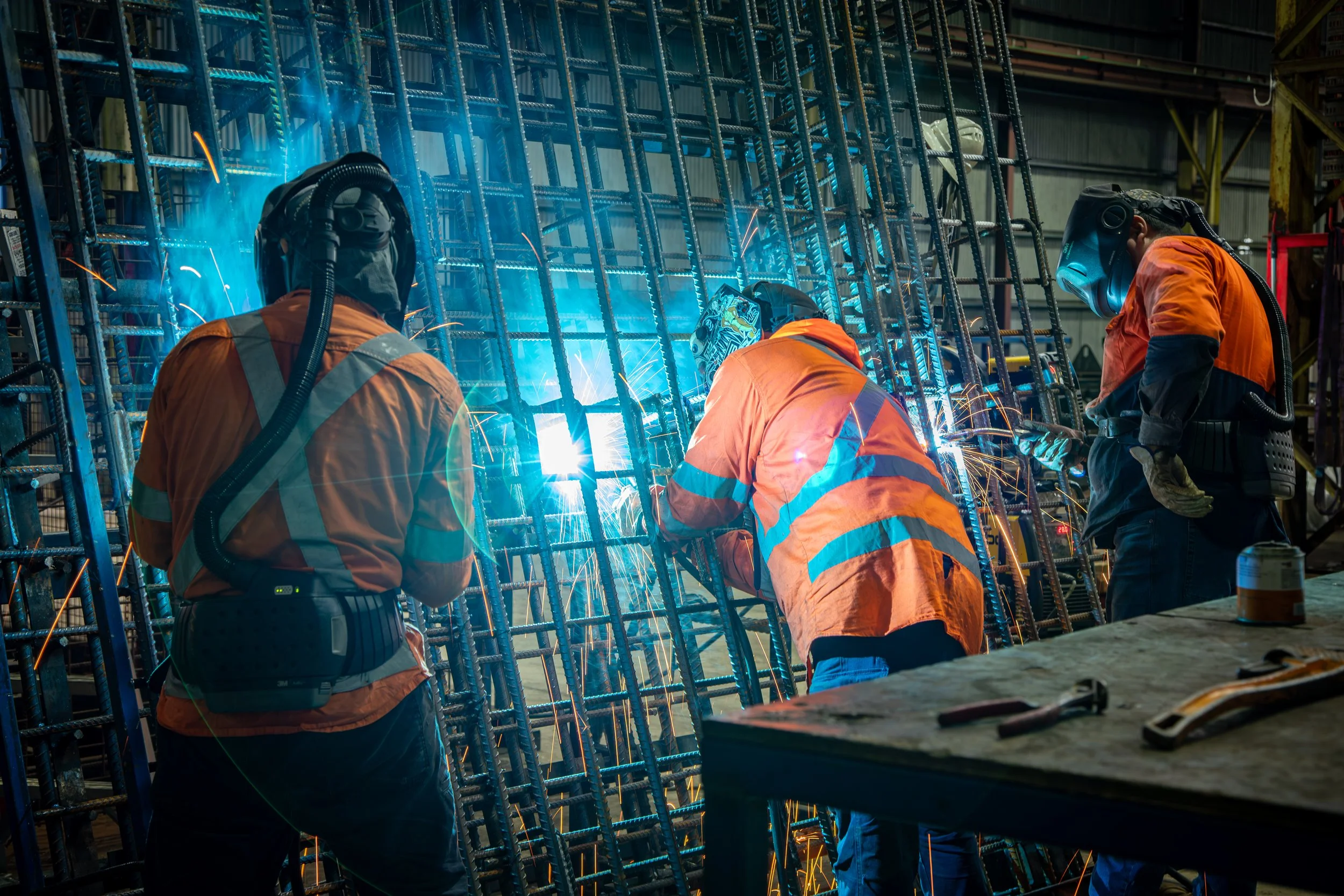 Team welding rebar structures with sparks flying at Carrabay steel fabrication workshop.