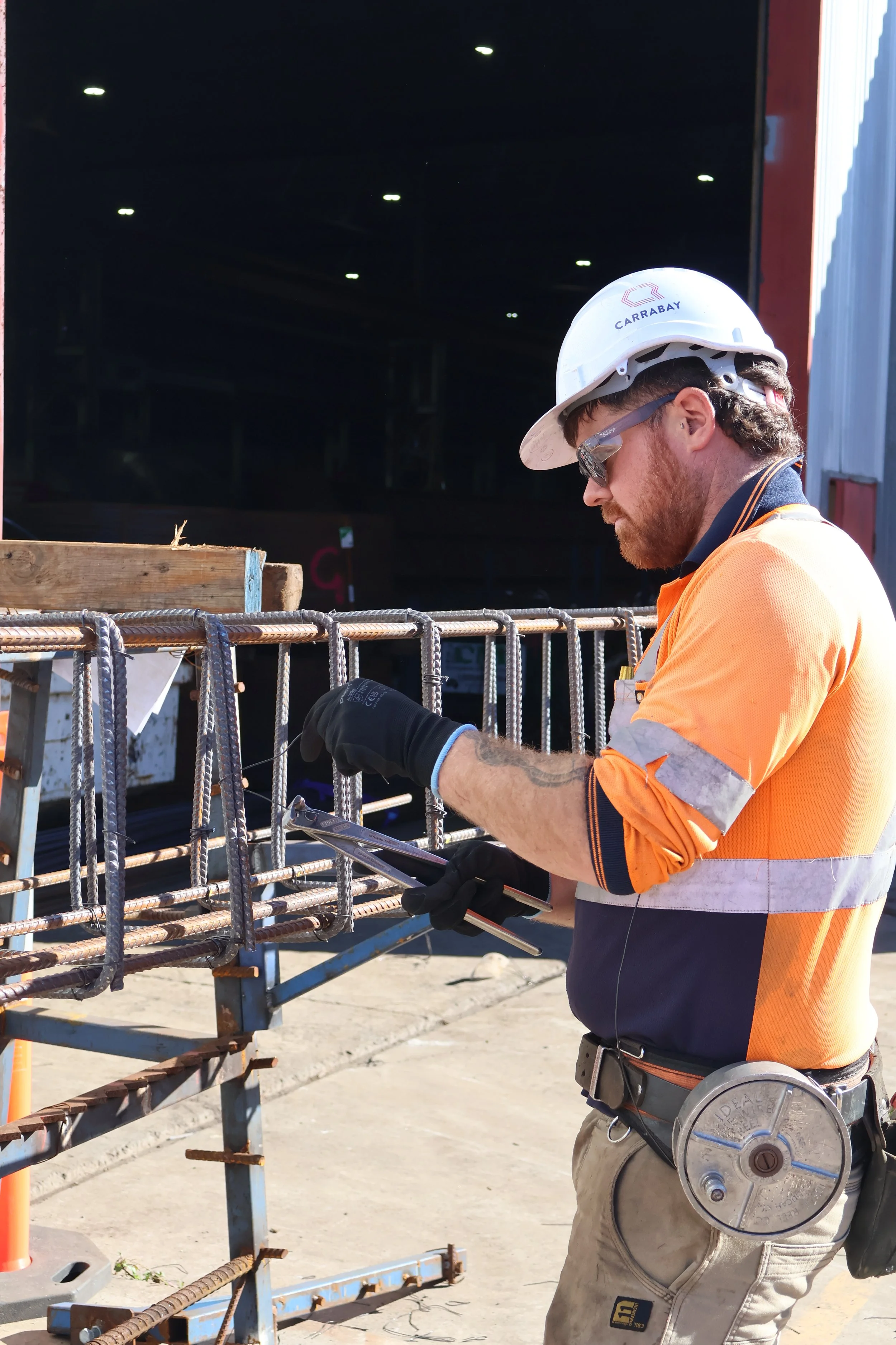 Construction worker in Carrabay PPE securing rebar for civil infrastructure project.