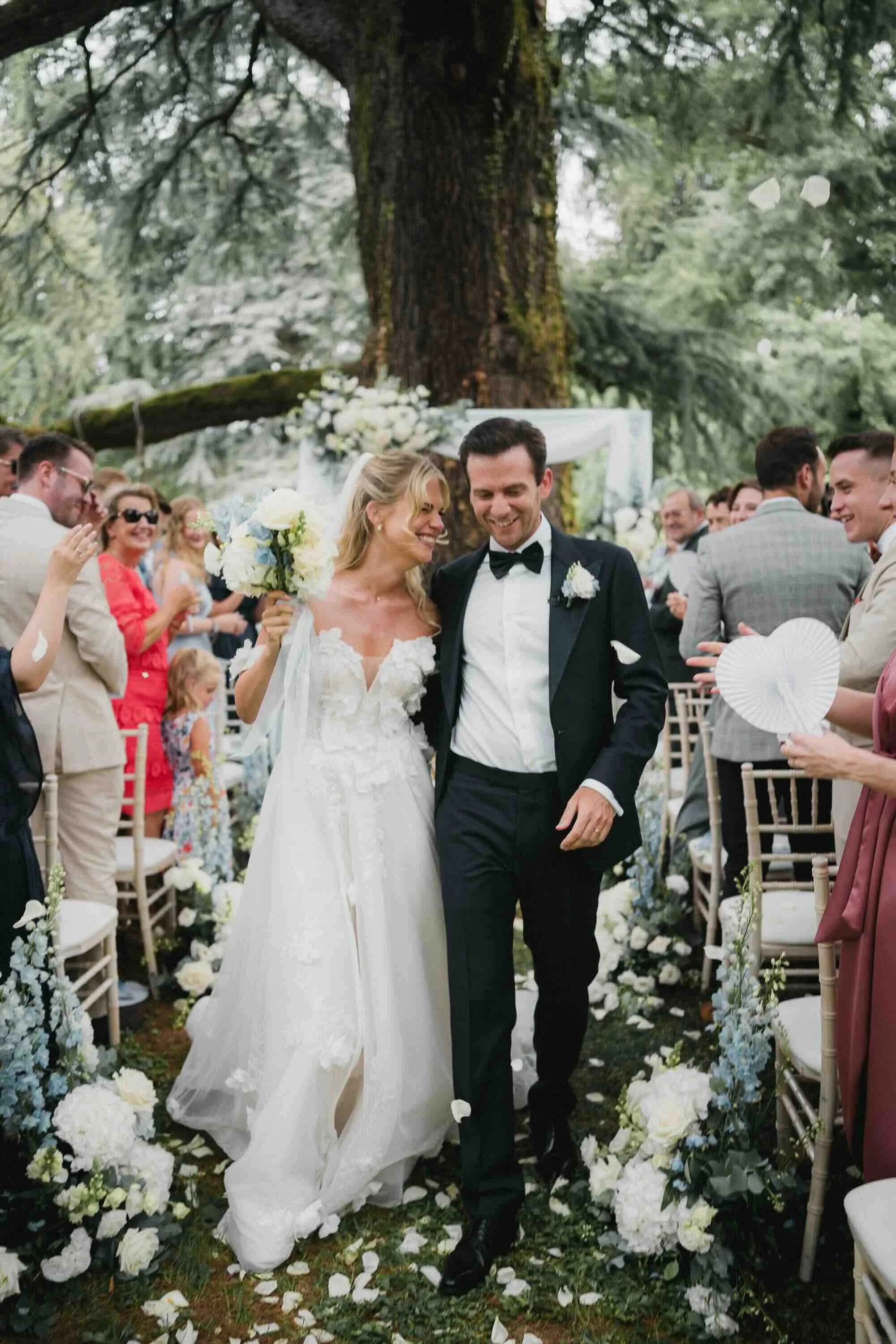 Bride and groom walking down the aisle at their outdoor wedding ceremony, surrounded by guests and floral decorations.