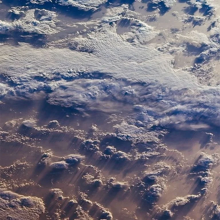View of Earth from space showing clouds and sunlight casting shadows.