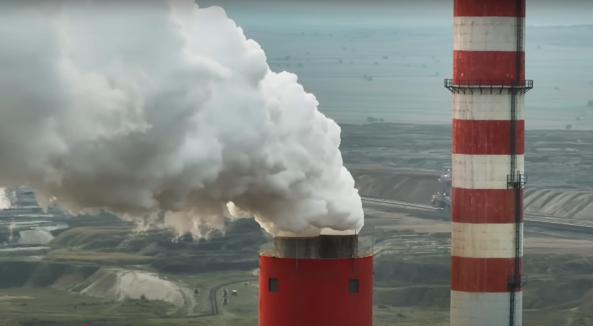Industrial smokestacks emitting white smoke at a power plant with a landscape background.