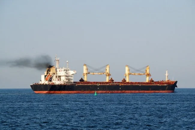 A large cargo ship sailing on the ocean with black smoke coming from the engine.
