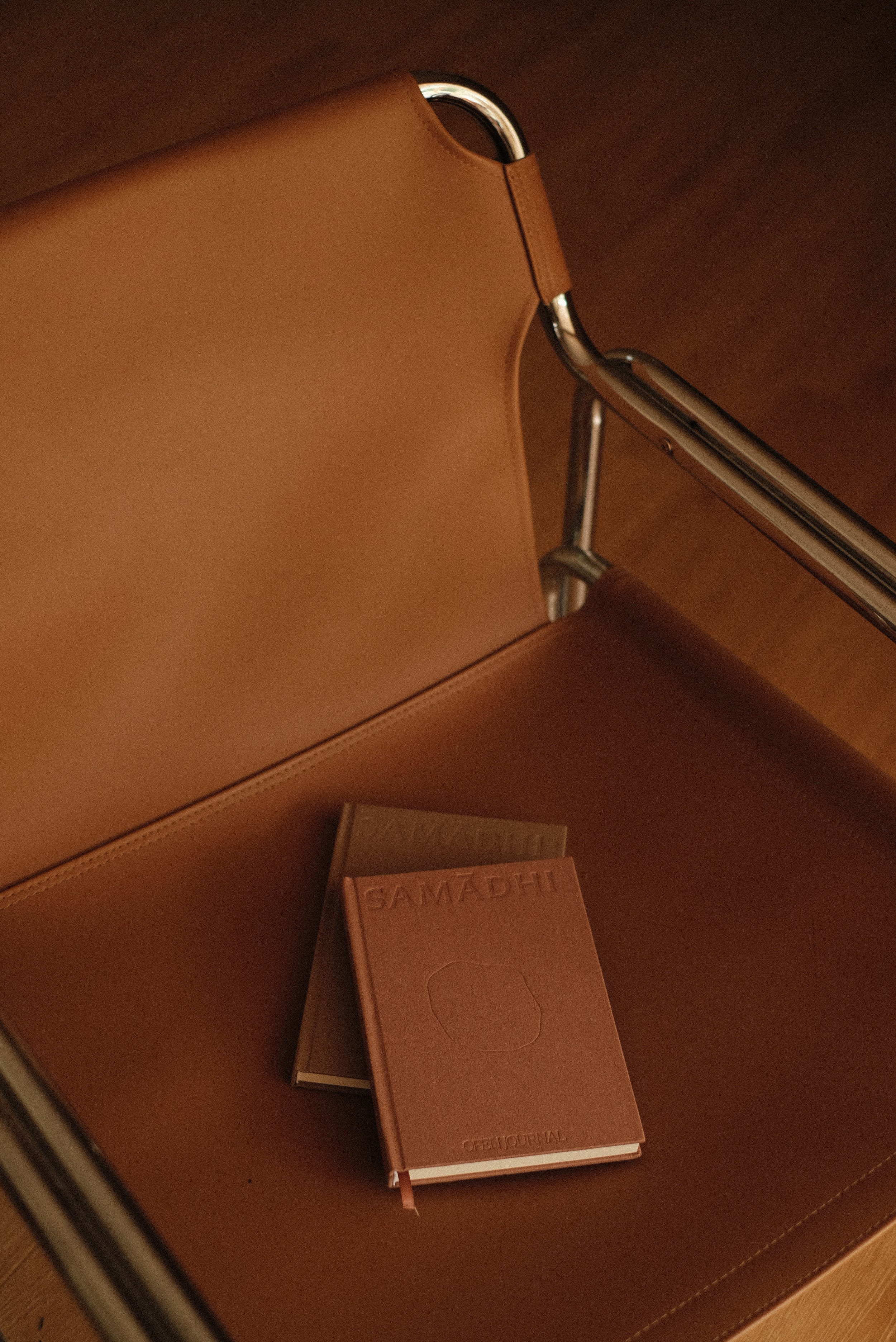 Two reflection journals, one of which is a gratitude journal, from the brand 'SAMADHI' on a tan leather chair.