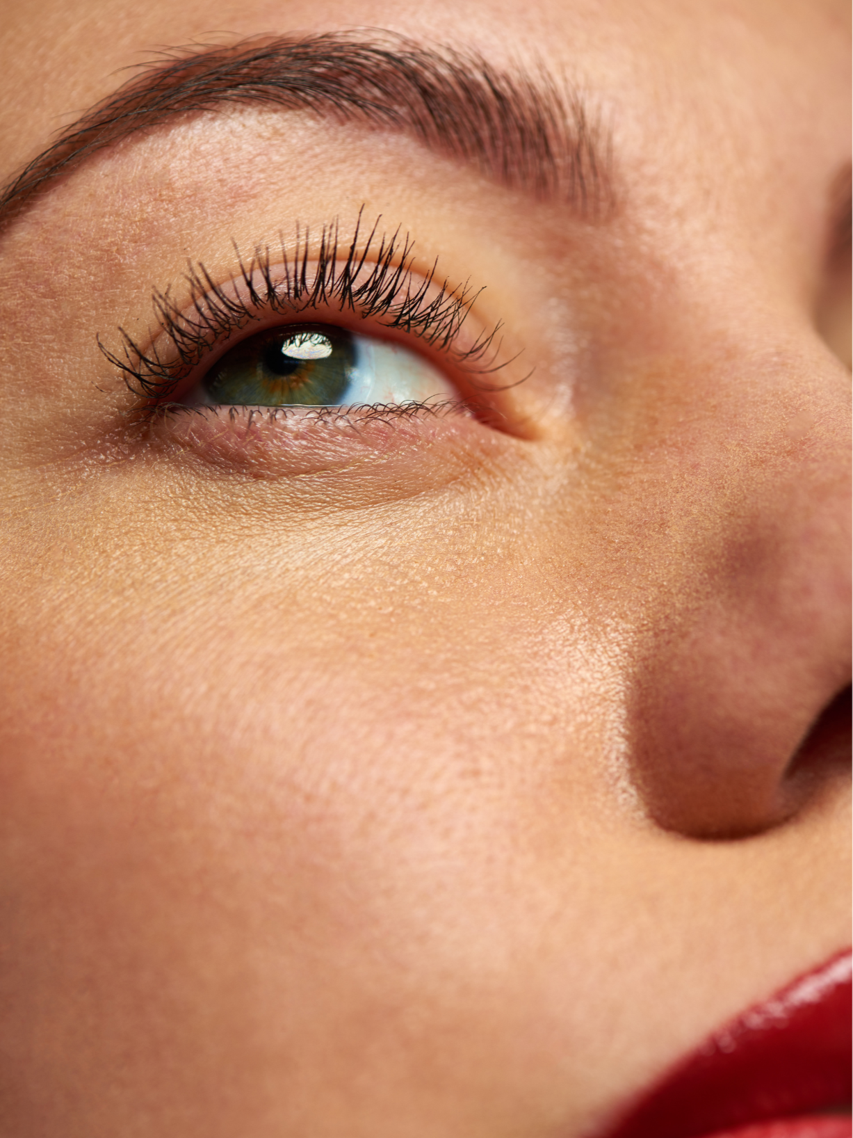 Close-up of a person's eye and part of their face, showing detailed skin texture, eyebrow, eyelashes, and blue-green eye.