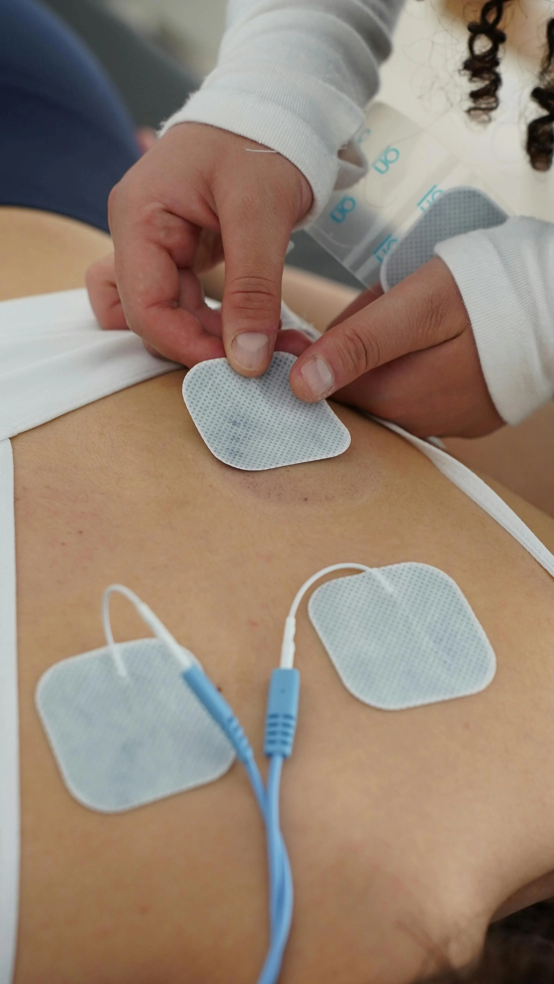 Eine Fachkraft bringt kleine Klebeelektroden auf der Haut einer Person an, um Muskelsignale für eine Biofeedback-Therapie zu erfassen.