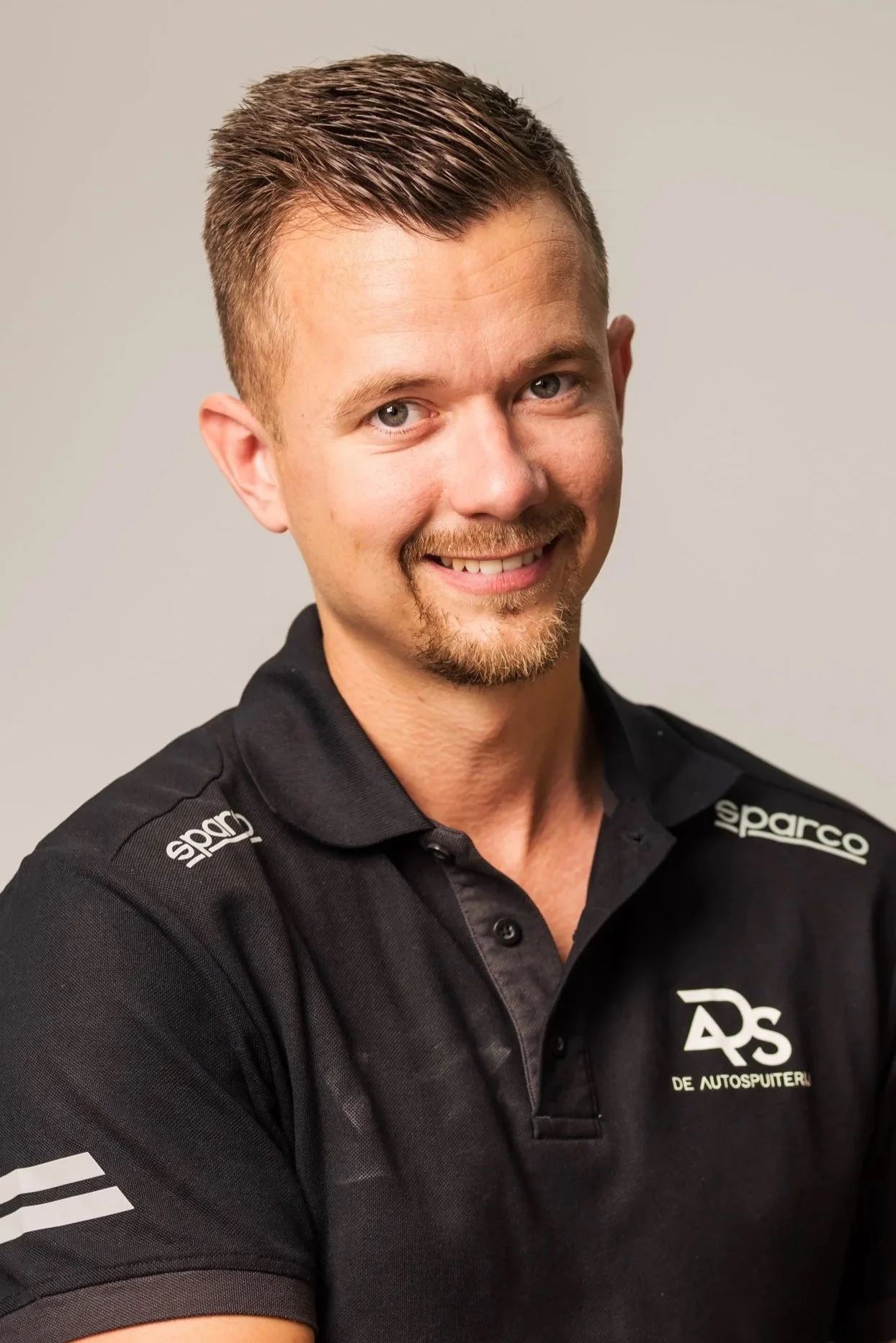 Mannen met kort haar, tatoeages, die zwarte handschoenen en een zwart autoreparatieshirt dragen, repareren een auto met afplaktape en verf in een garage.
