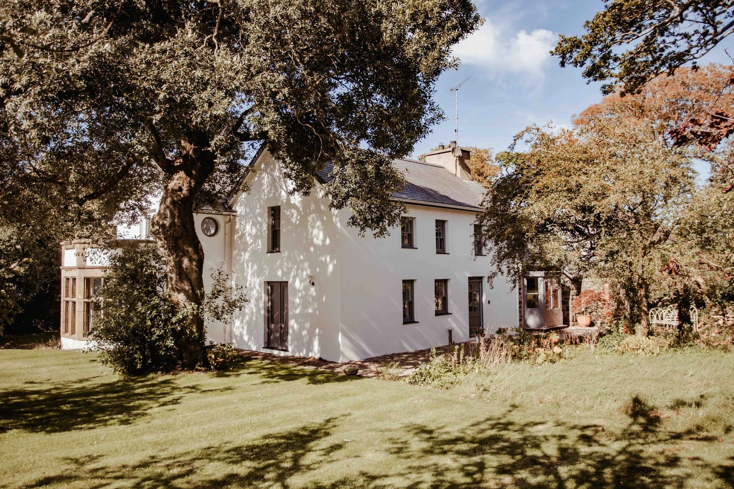 A white house with multiple windows surrounded by large trees and a grassy yard.