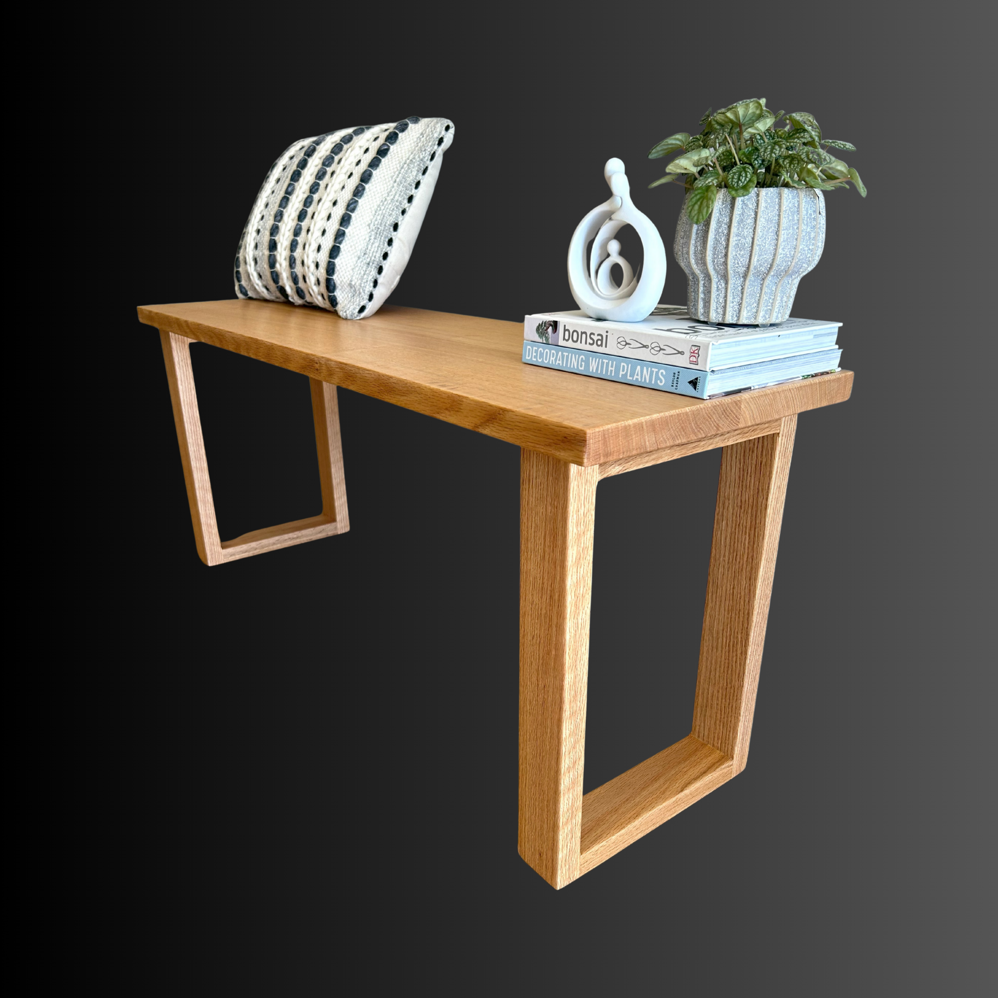 A wooden table with decorative items including a cushion, a potted plant, a sculpture, and books, set against a gray background.