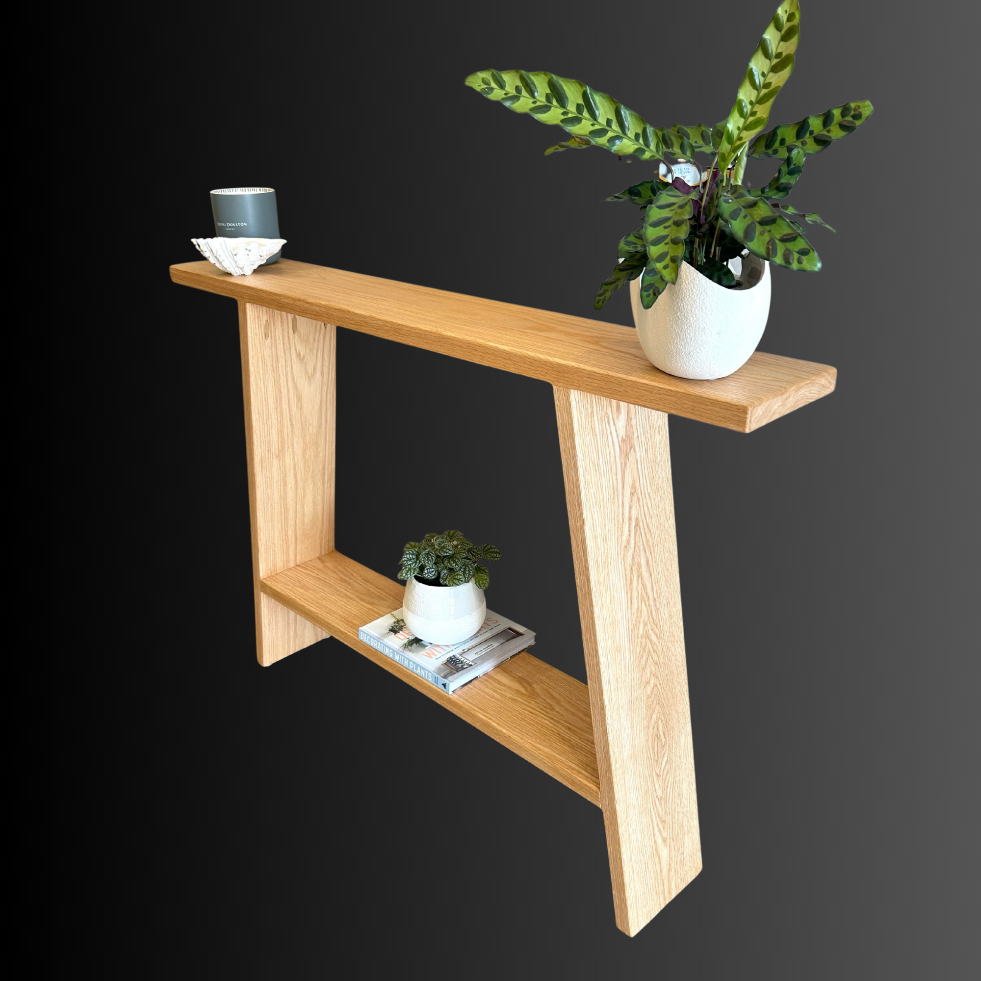 A wooden shelf with two levels, decorated with potted plants and small decorative objects, against a dark background.