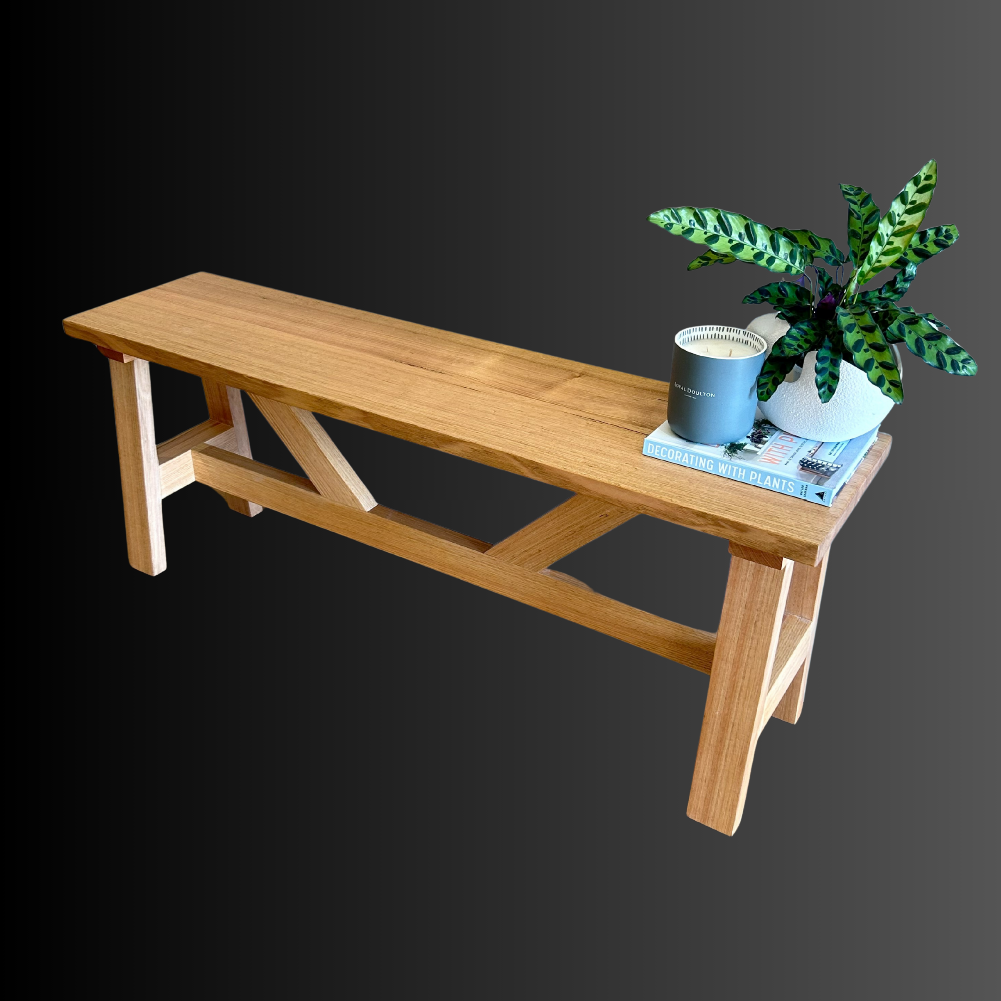 A wooden bench with a green potted plant, a candle, and a book on top, set against a gradient background.