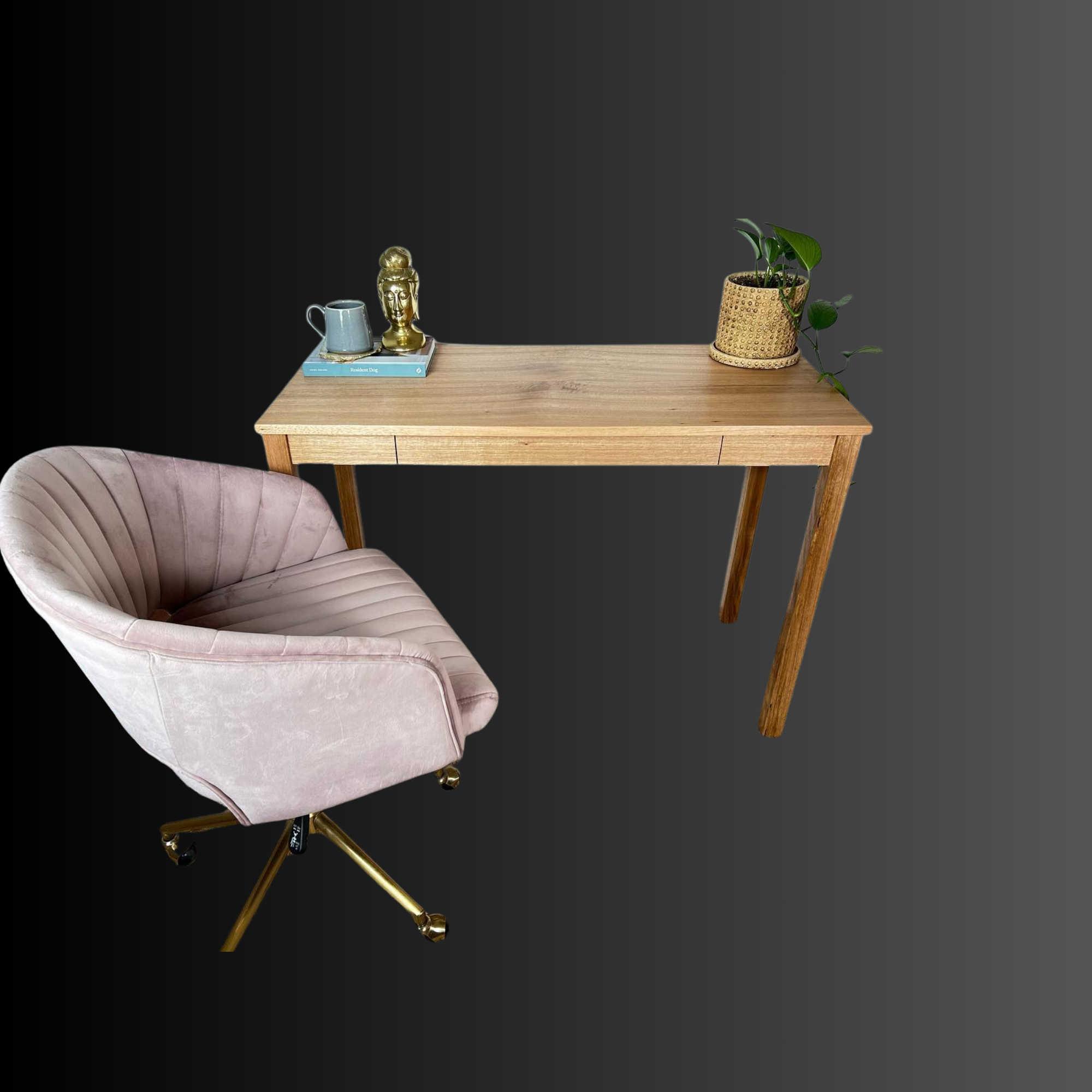 A pink velvet swivel chair with gold legs placed next to a wooden desk with a potted plant, a decorative sculpture, and books on a black and gray background.