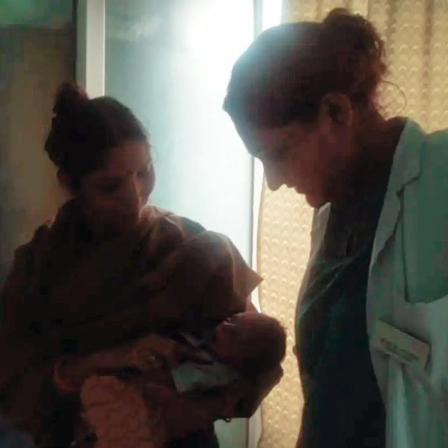 A woman holding a newborn baby and a healthcare professional in a hospital room with soft lighting.