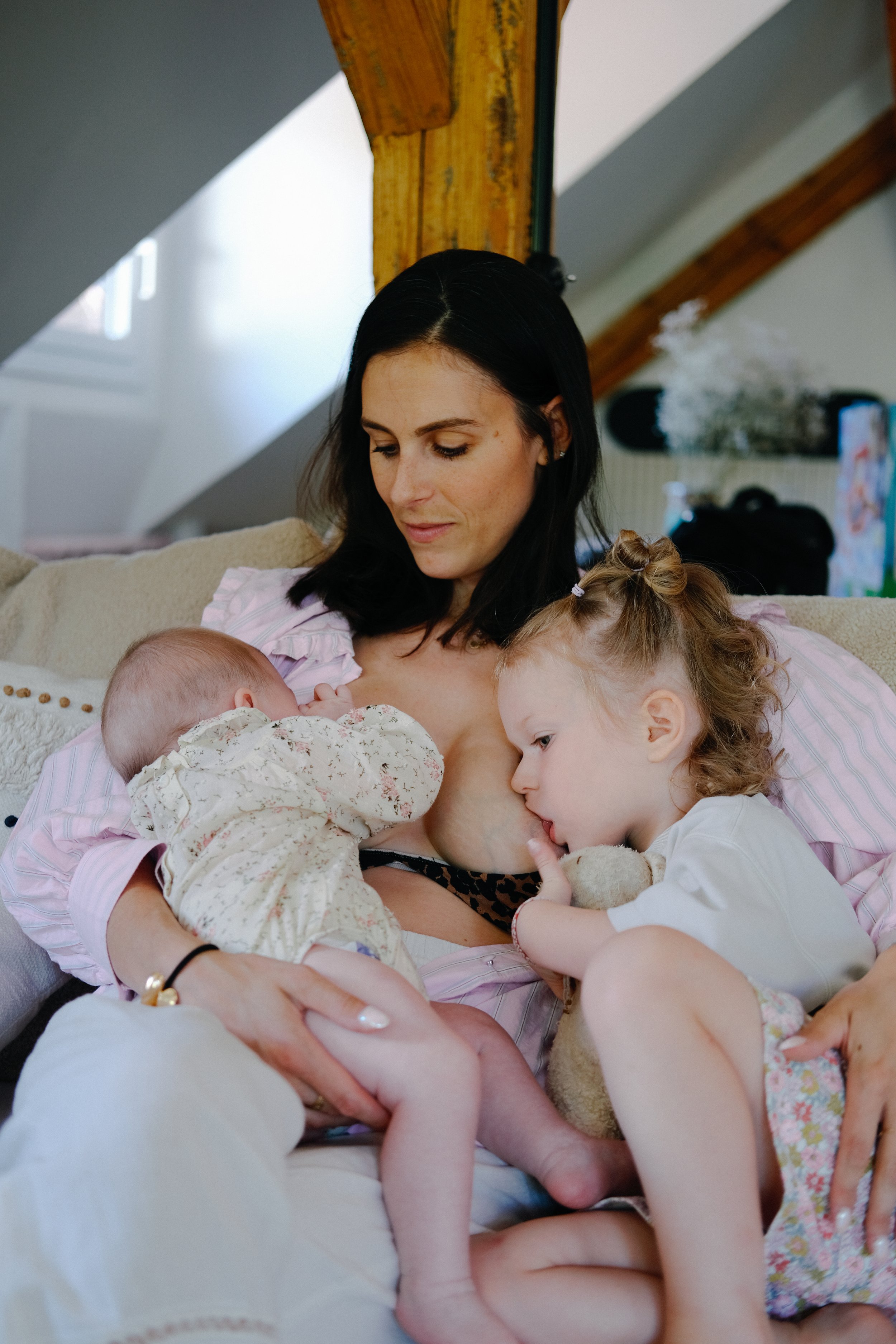 Une femme avec deux jeunes enfants, une fille aux cheveux bouclés. Ils sont tous en train d'allaiter ou de nourrir de façon intime, dans un cadre familial confortable et chaleureux.