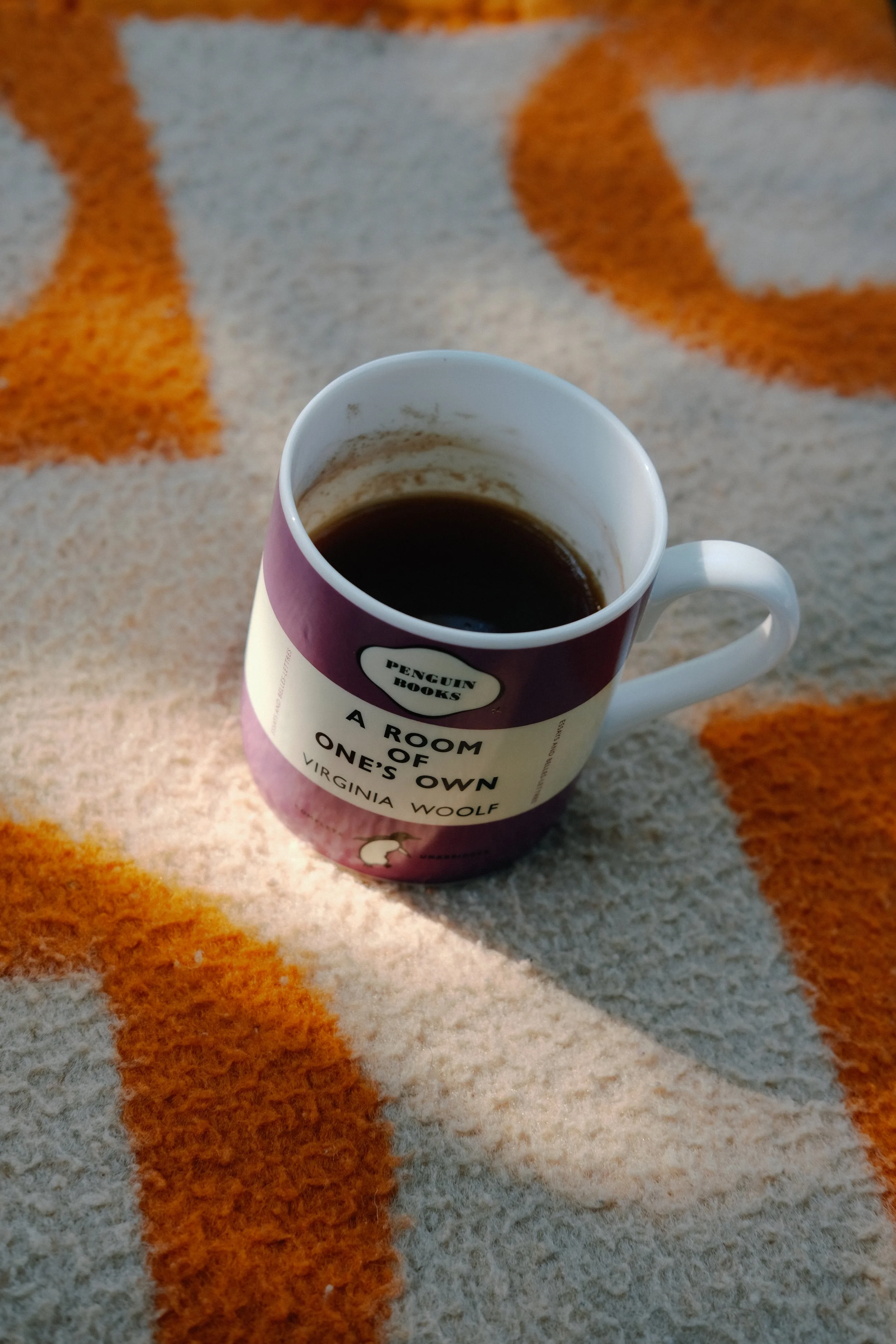 Tasse de café noir posée sur un tapis à motif orange, blanc et beige.