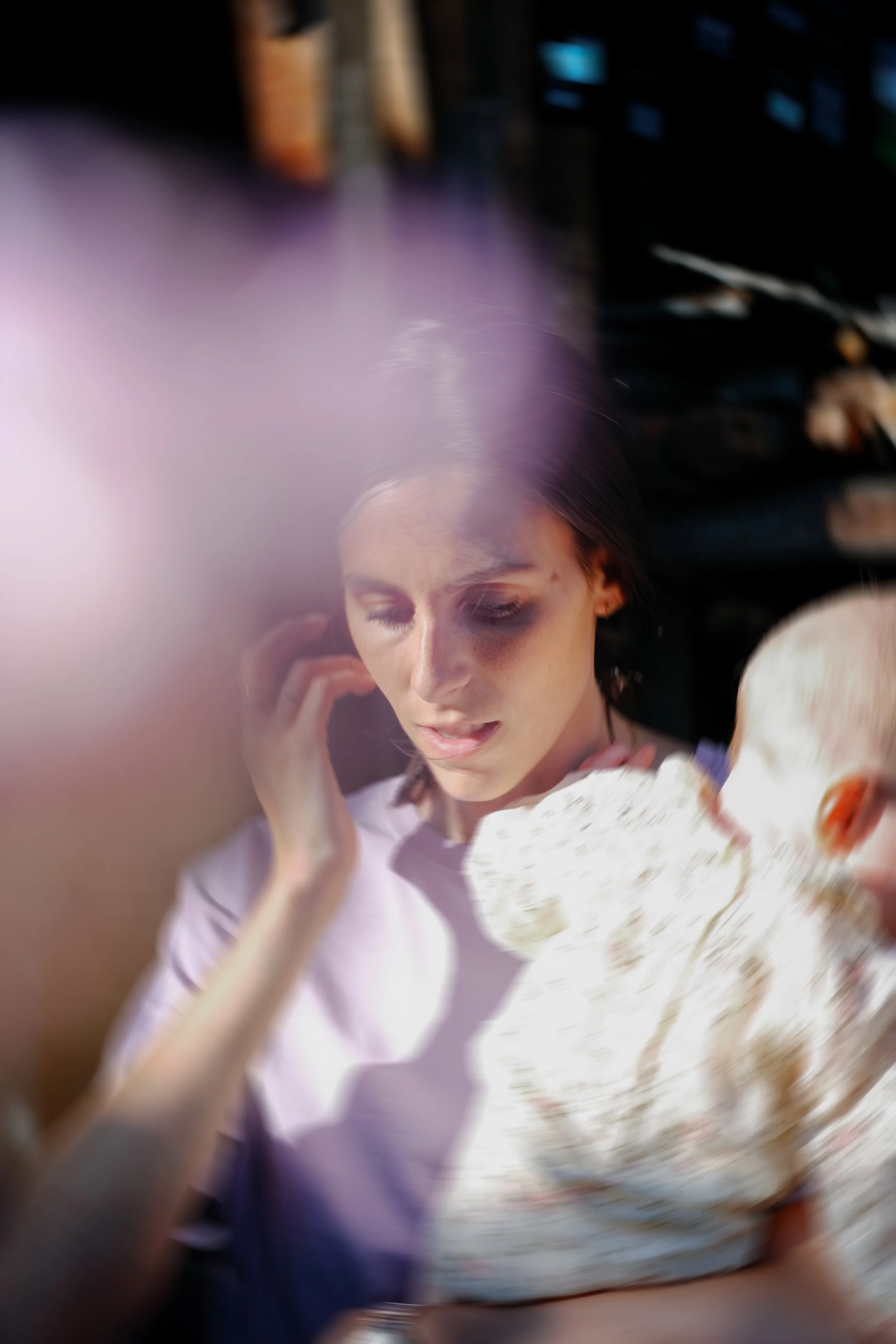 Une femme aux cheveux bruns, portant un t-shirt blanc, est en train de regarder légèrement vers le bas dans un environnement lumineux, avec un flou artistique autour d'elle.