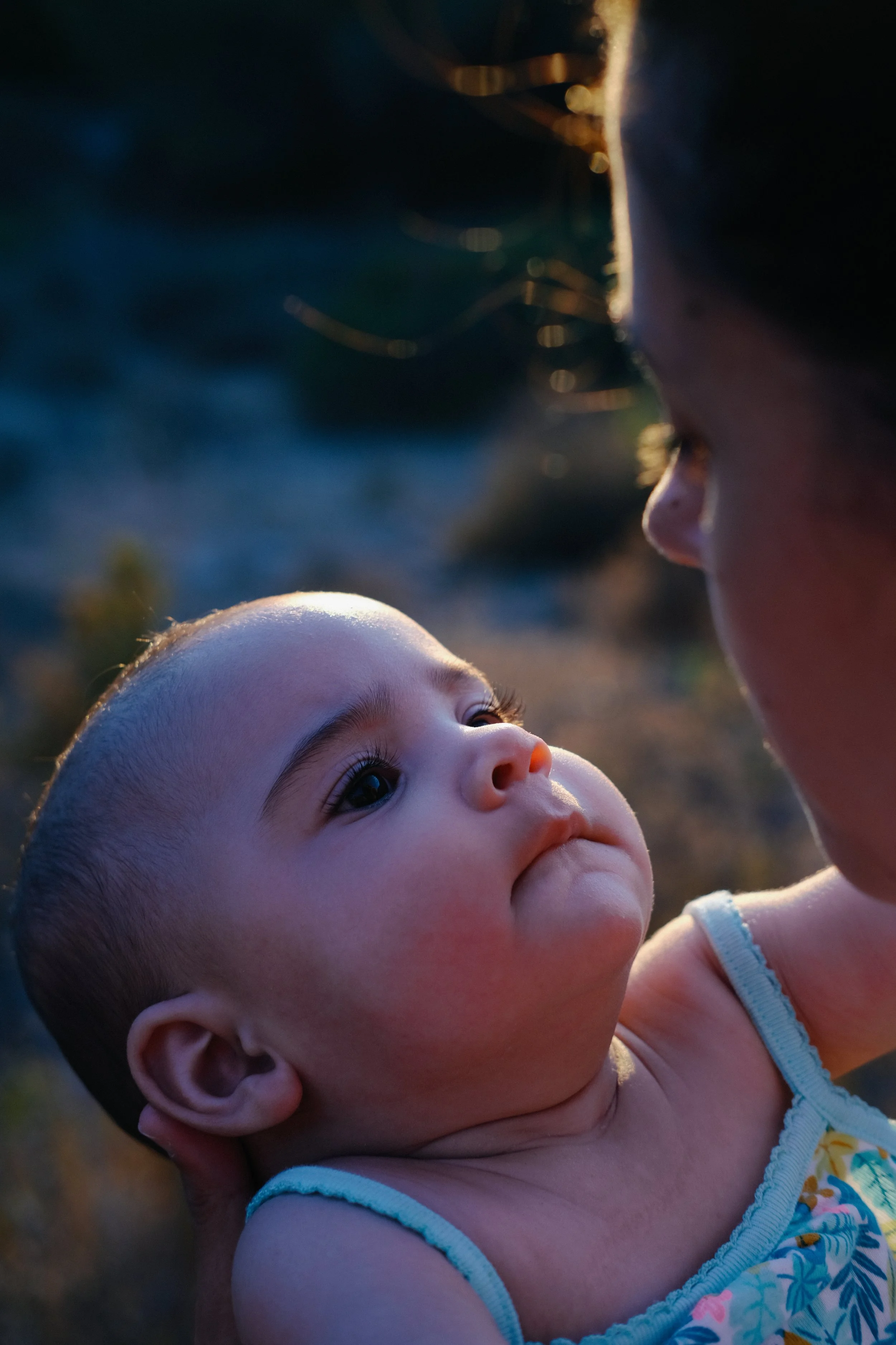 Un adulte et un bébé regardant l'un l'autre dans un éclairage doux, probablement au coucher du soleil.
