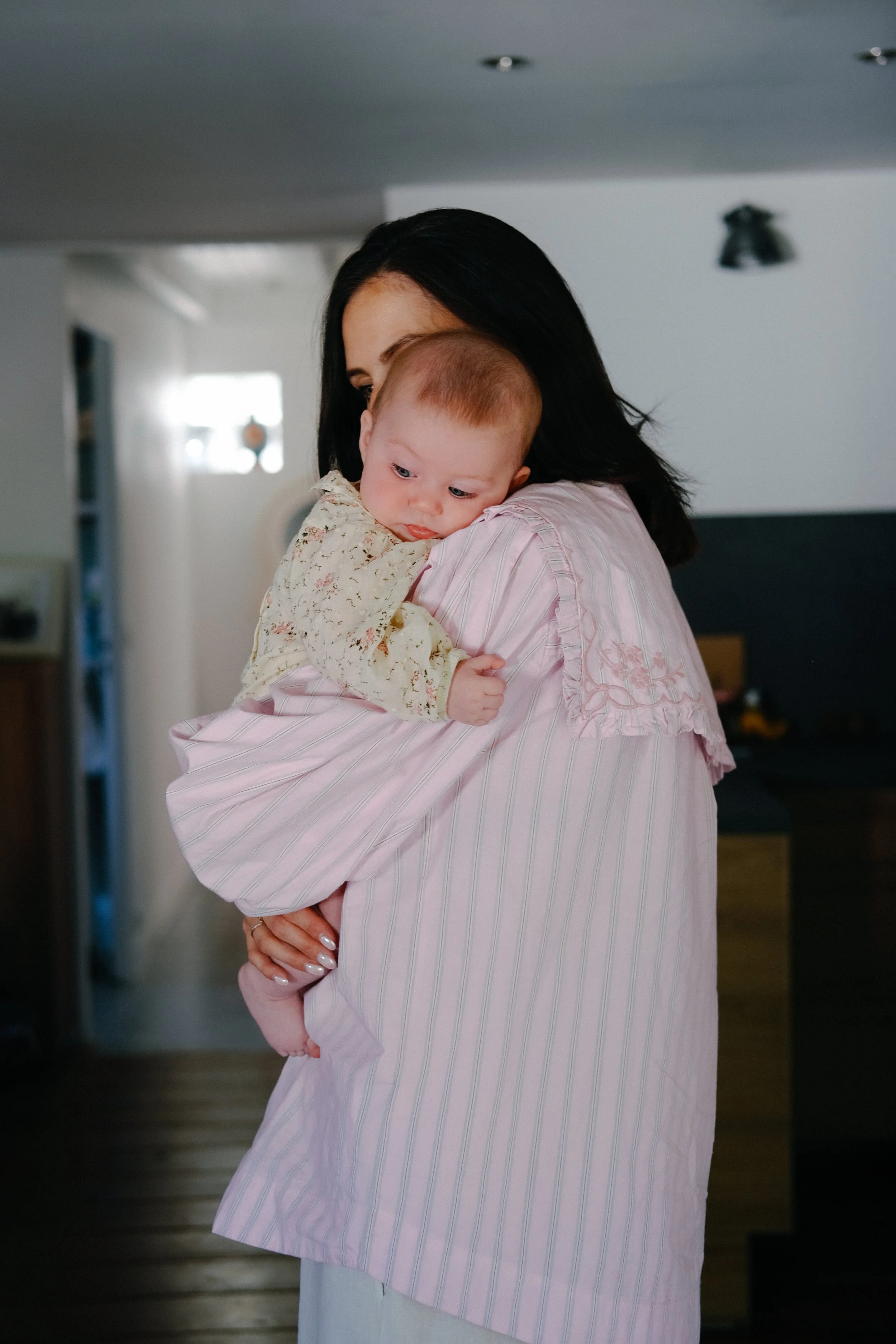 Une femme avec des cheveux noirs court tenant un bébé dans ses bras, dans un intérieur domestique.