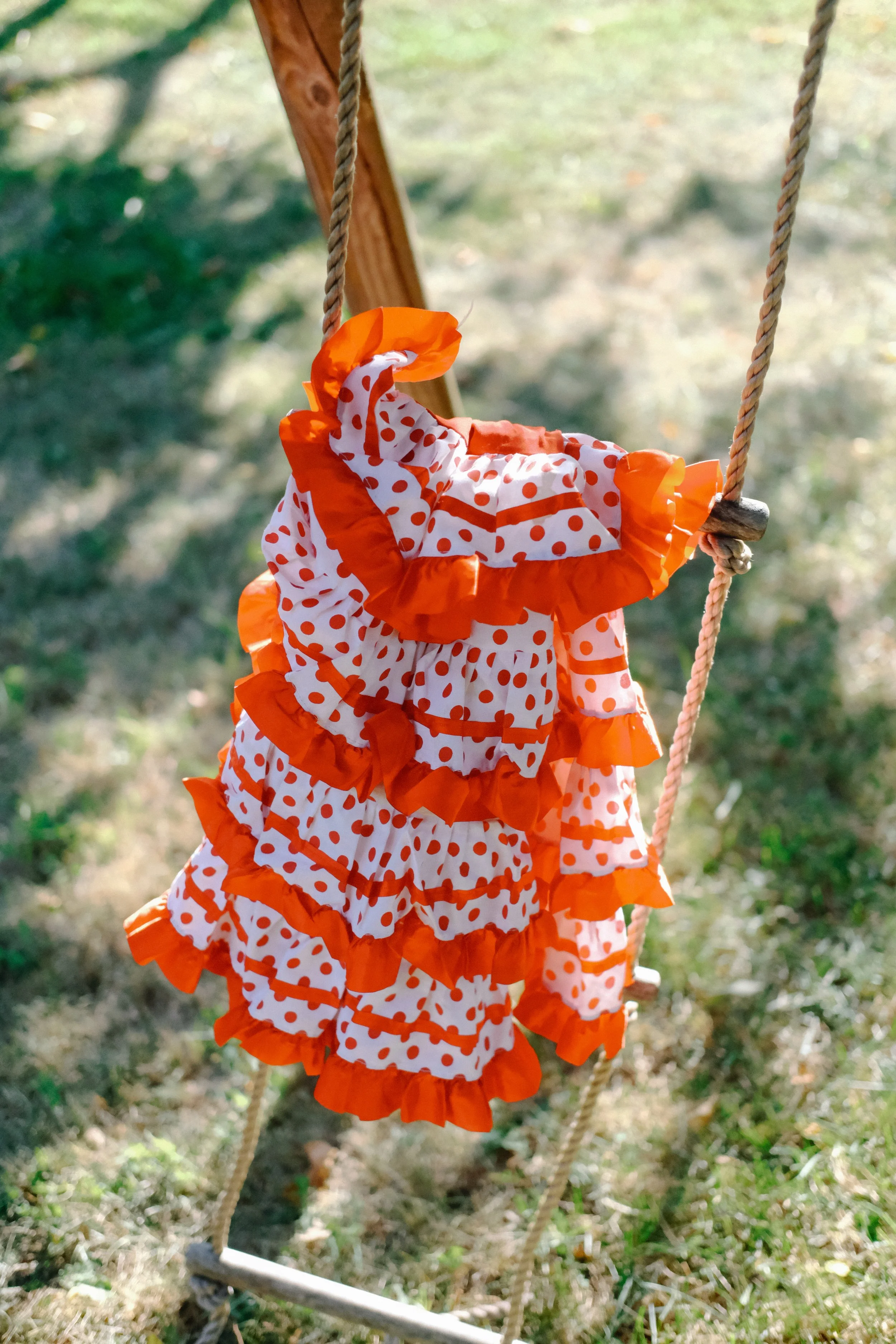 Mobiles avec une robe à pois rouges et blanches sur une balançoire en bois dans un parc extérieur.