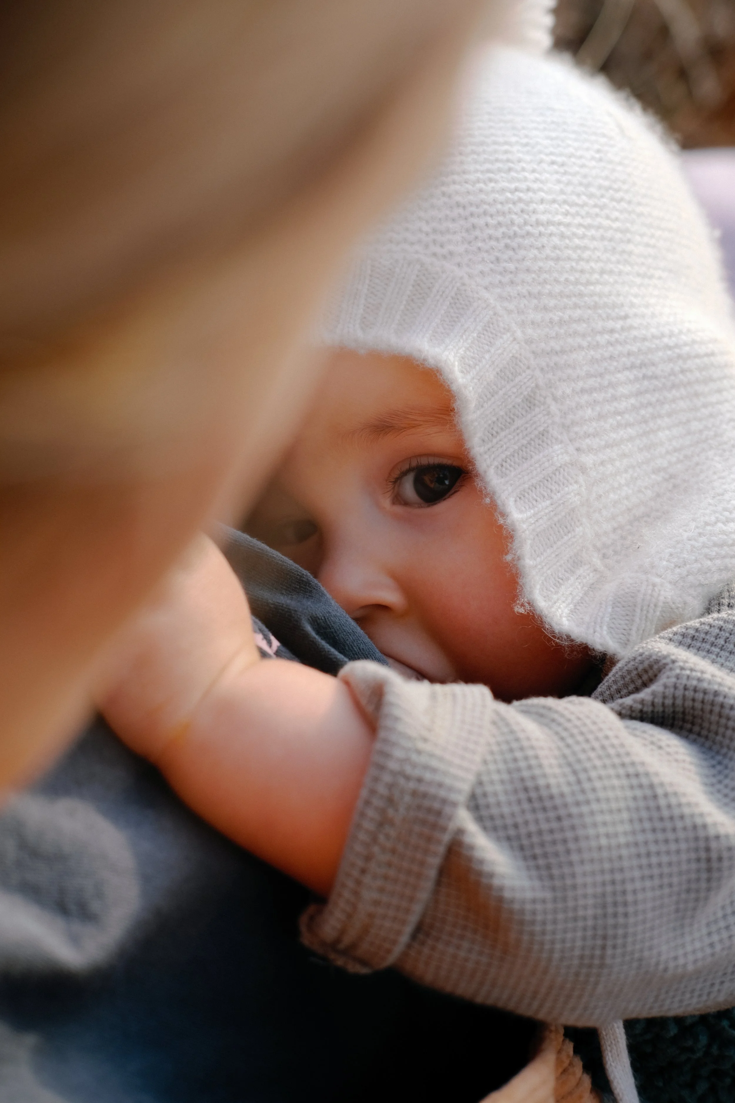 Un bébé portant un bonnet blanc, partiellement visible, regarde l'objectif avec une expression calmement curieuse.