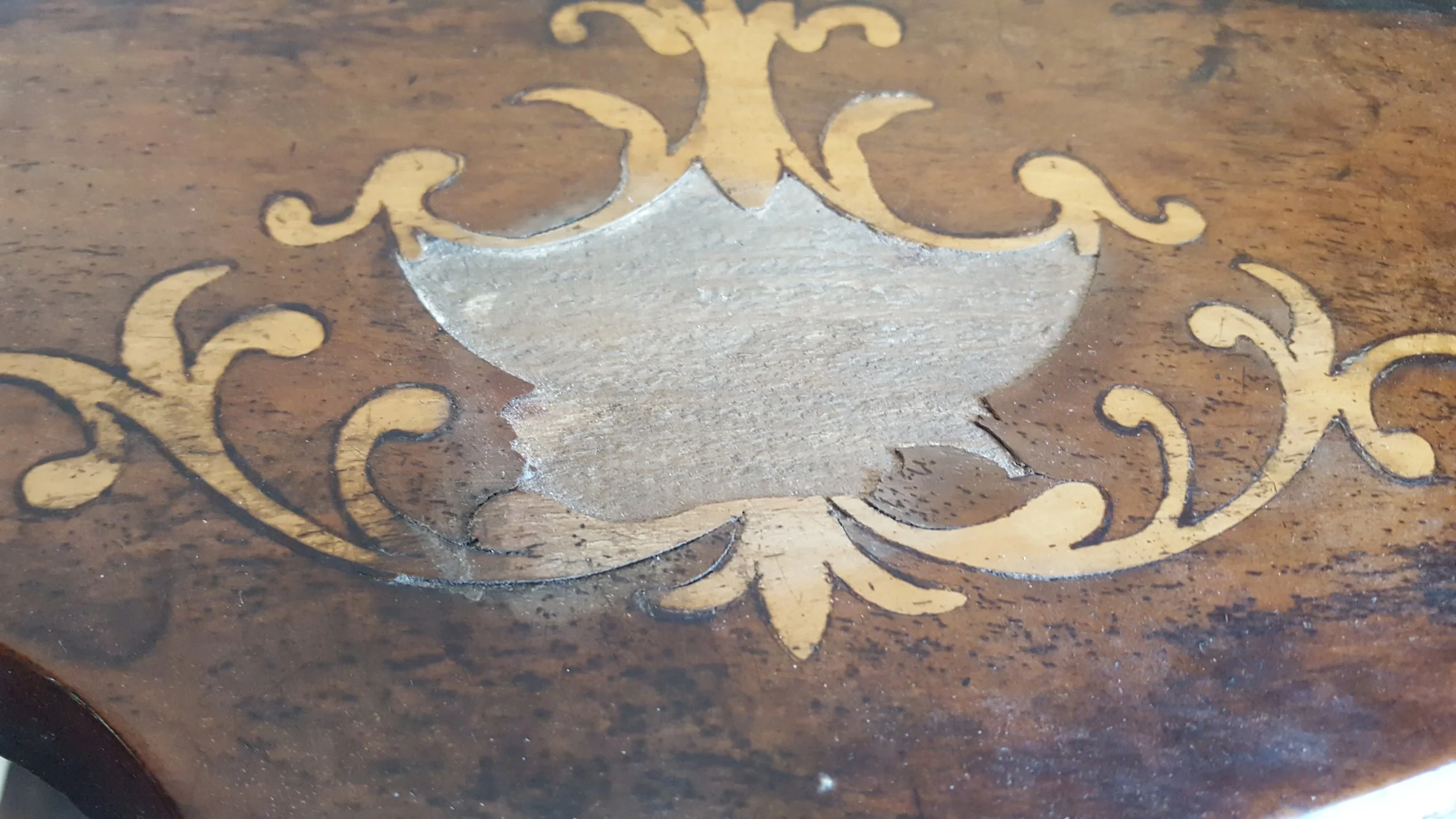 Close up view showing damage to the Marquertry inlay of a shelf of a Victorian whatknot