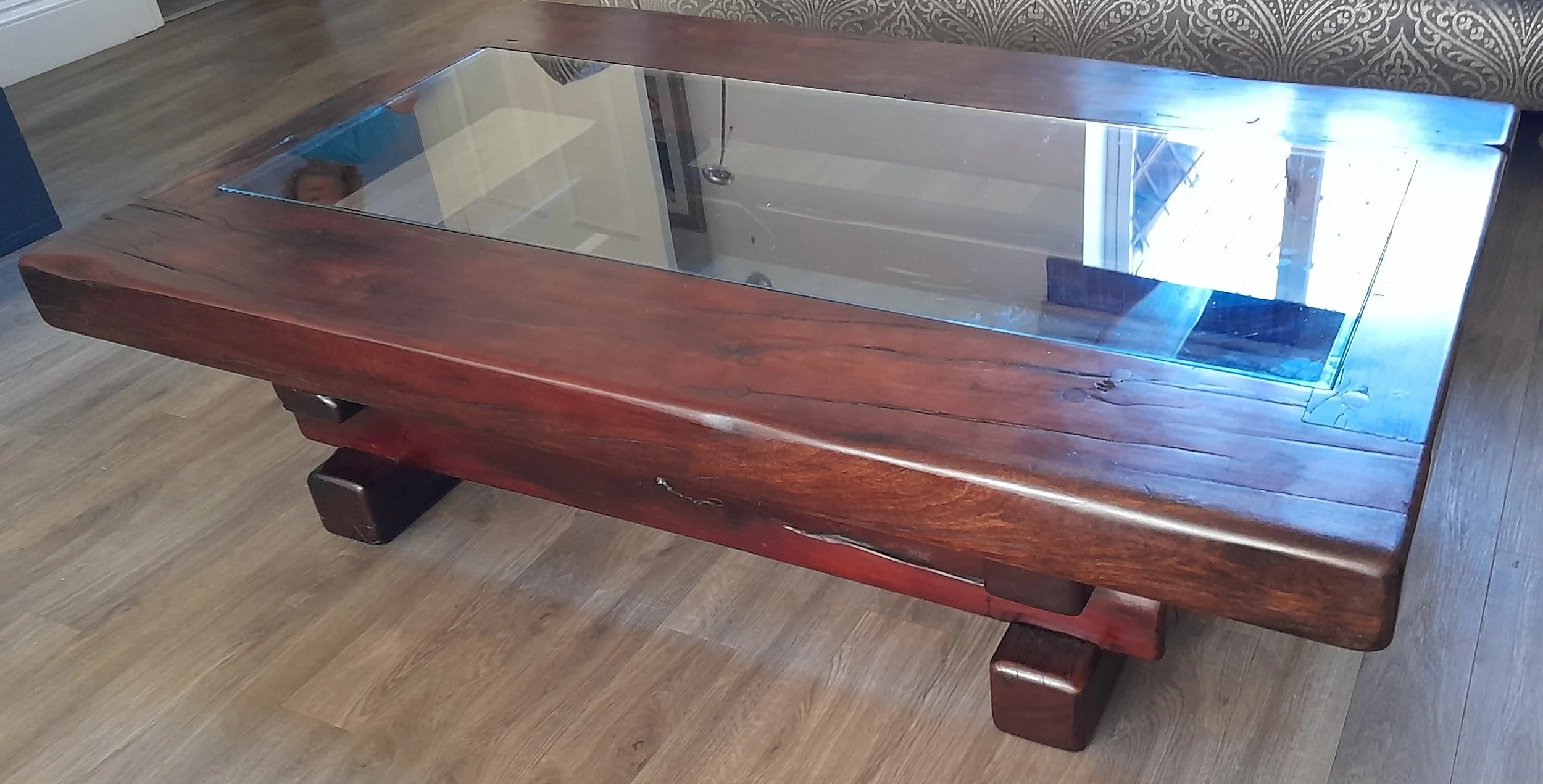 A wooden coffee table with a glass top, situated on a brown wood floor.