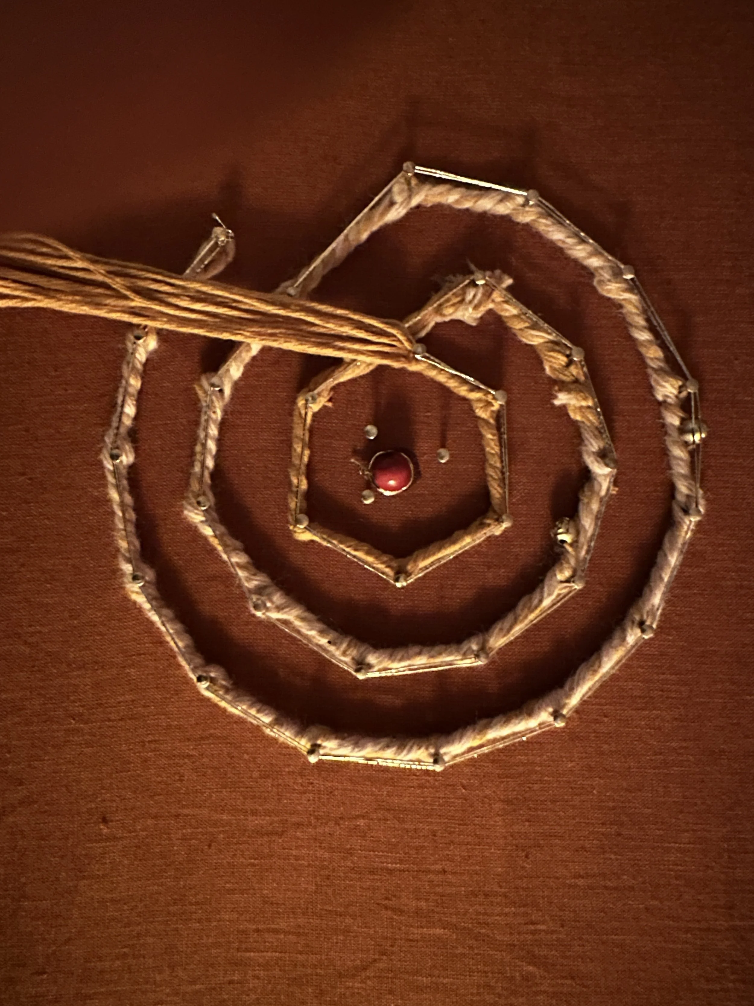 Jewelry arranged in a spiral pattern on a brown surface, including a red gemstone ring and a necklace with multiple strands.