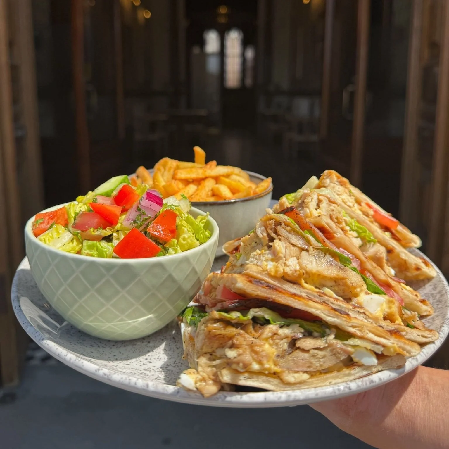 Plate with club sandwiches, side salad, and French fries inside the doorway to Riad Brunch Cafe at The Parrs Bank Hotel.