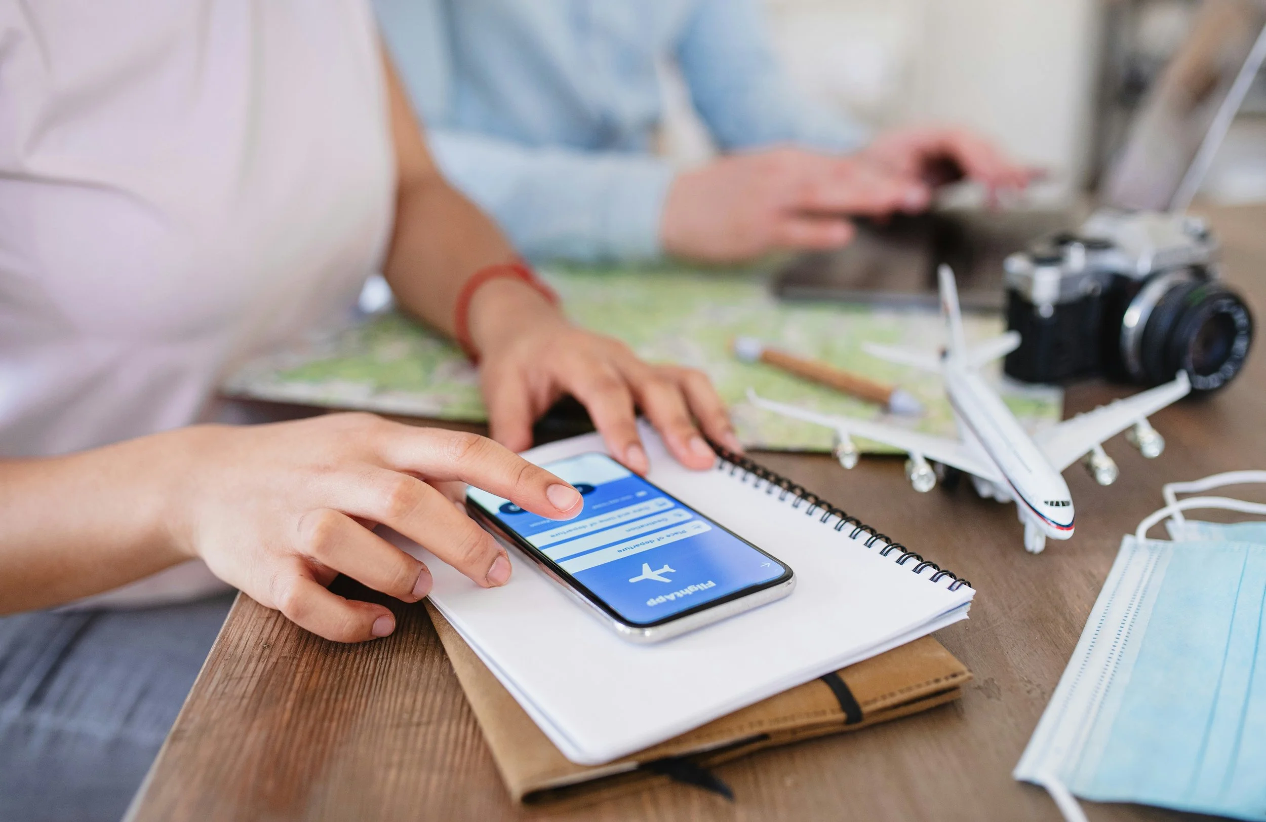 Traveler using a smartphone to plan flights beside a notebook, model airplane, and camera.  Copy