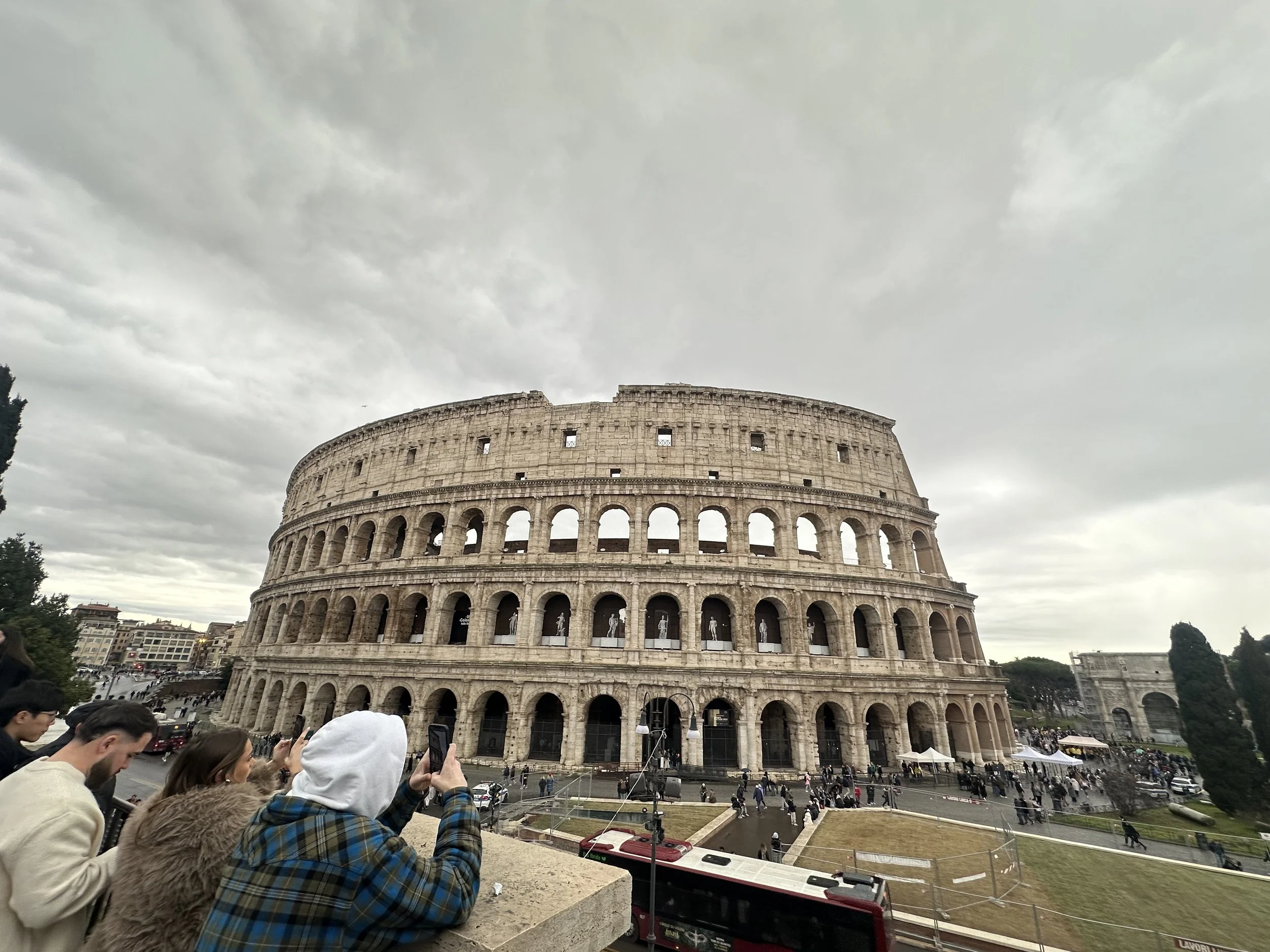 People taking photos of the Colosseum in Rome, Italy on a cloudy day.