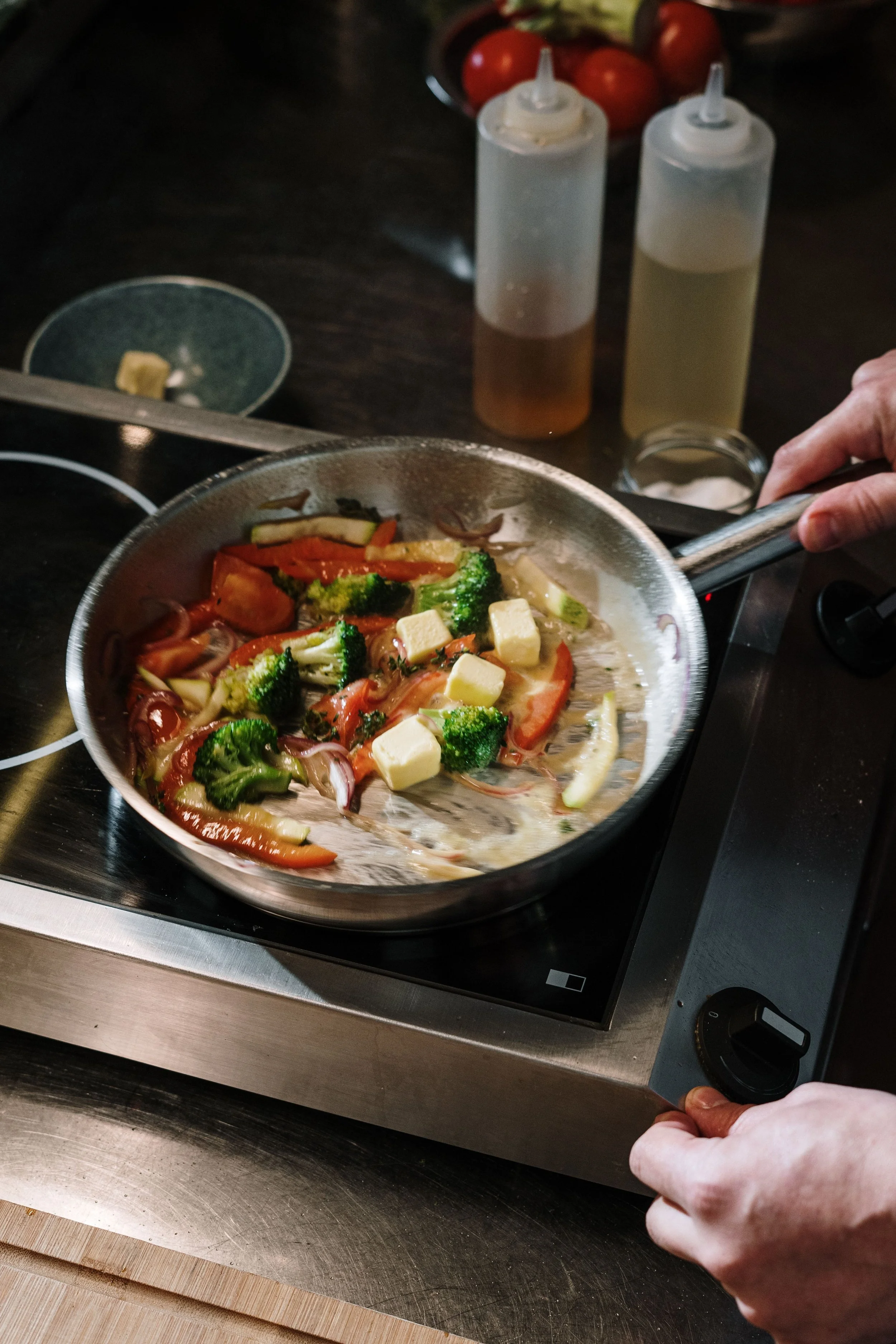 Someone cooking a stir fry with broccoli, tomato's, peppers, and tofu. 