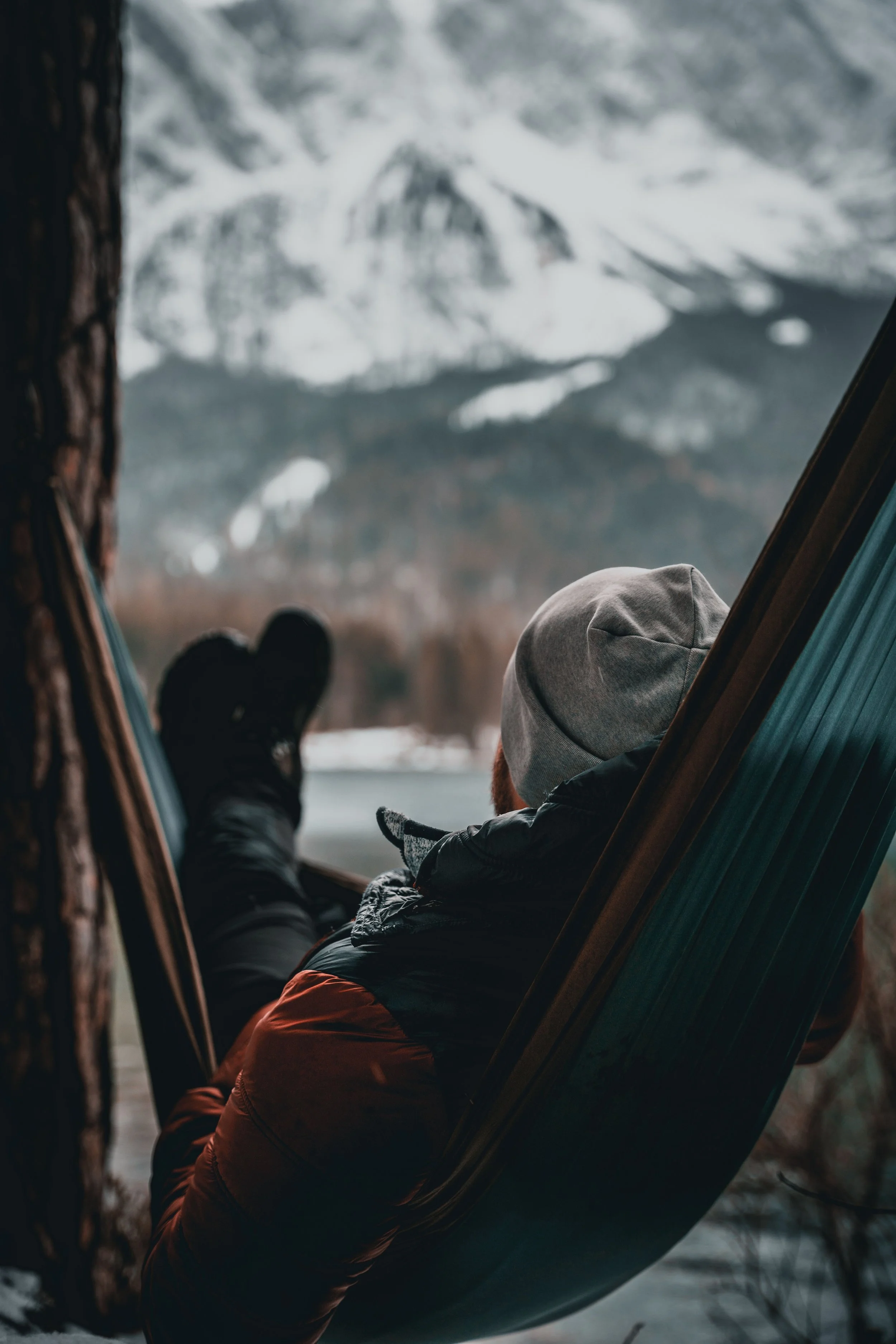 A man relaxing in a hammock in the winter looking out to snow covered mountains.
