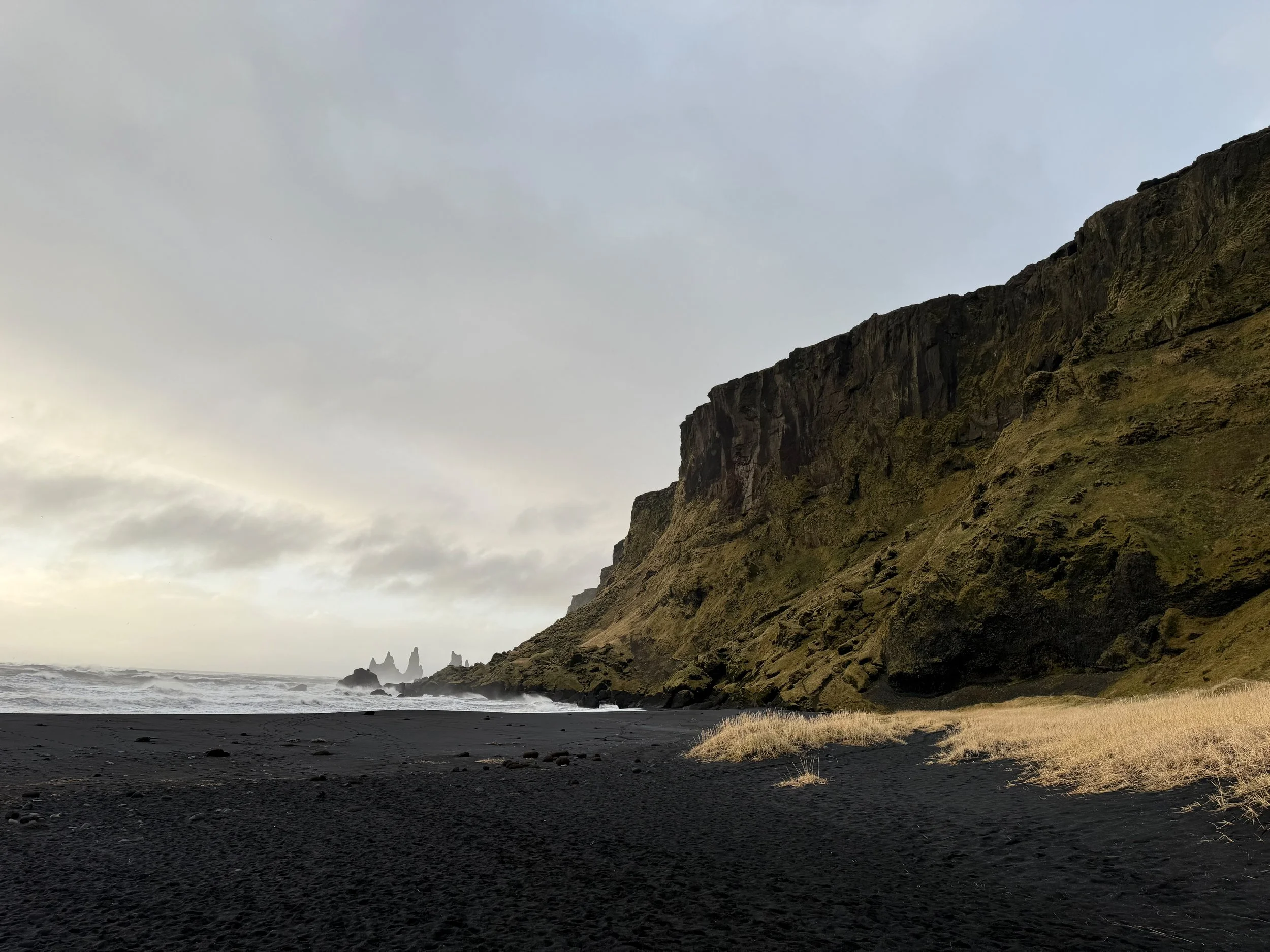 Black sand beach in Iceland with ocean waves crashing on the left and a green mountain on the right.