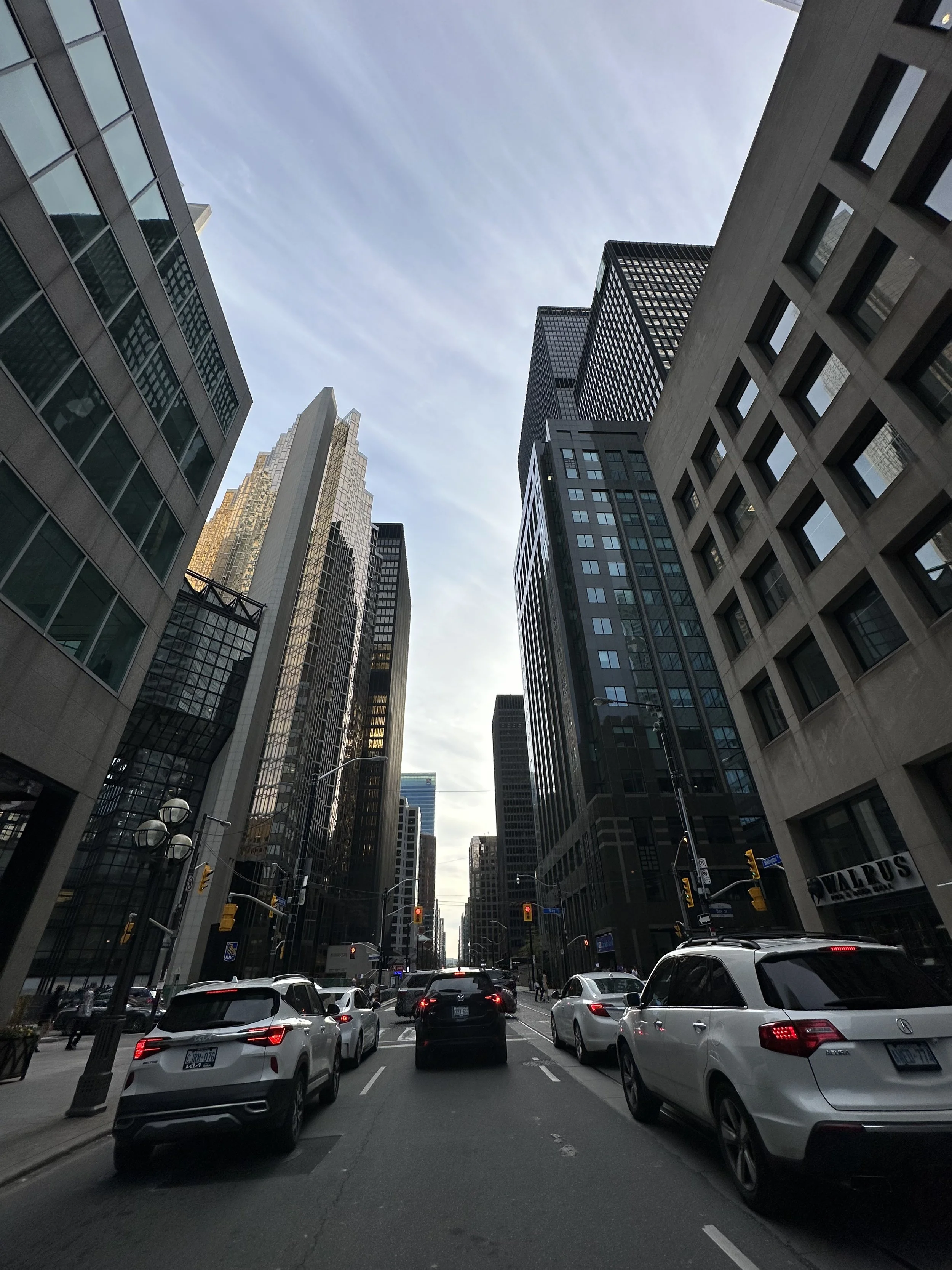 City street with tall buildings on both sides and vehicles stopped at traffic lights.