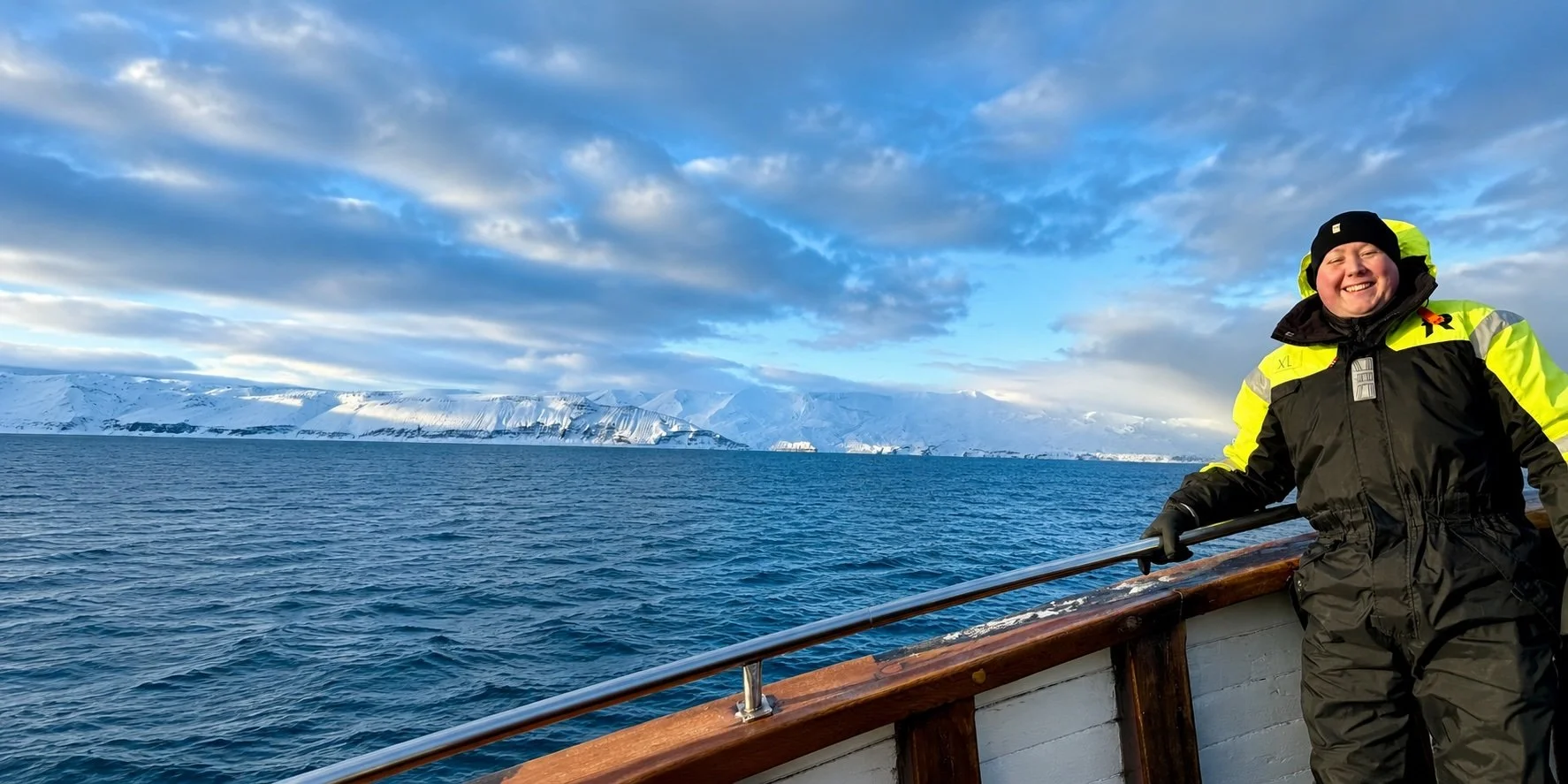 The founder of Glucose Getaways on a wooden boat whale watching in the winter in Iceland with large glacier in the background.