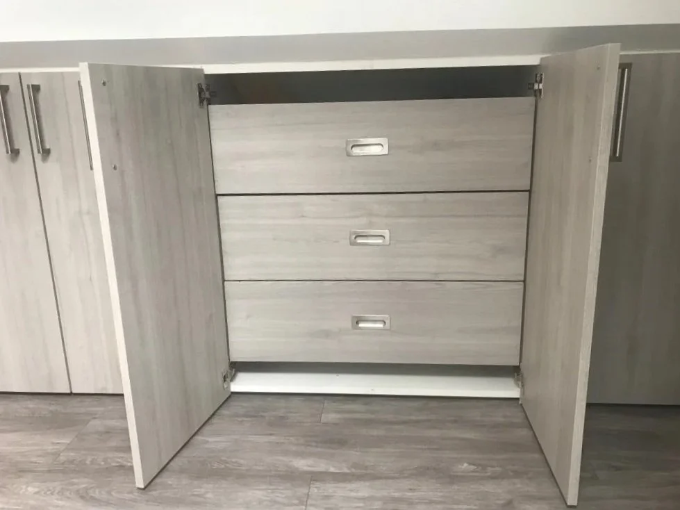 Une commode en bois clair avec trois tiroirs, placée à l'intérieur d'une armoire avec deux portes ouvertes, dans un style moderne.