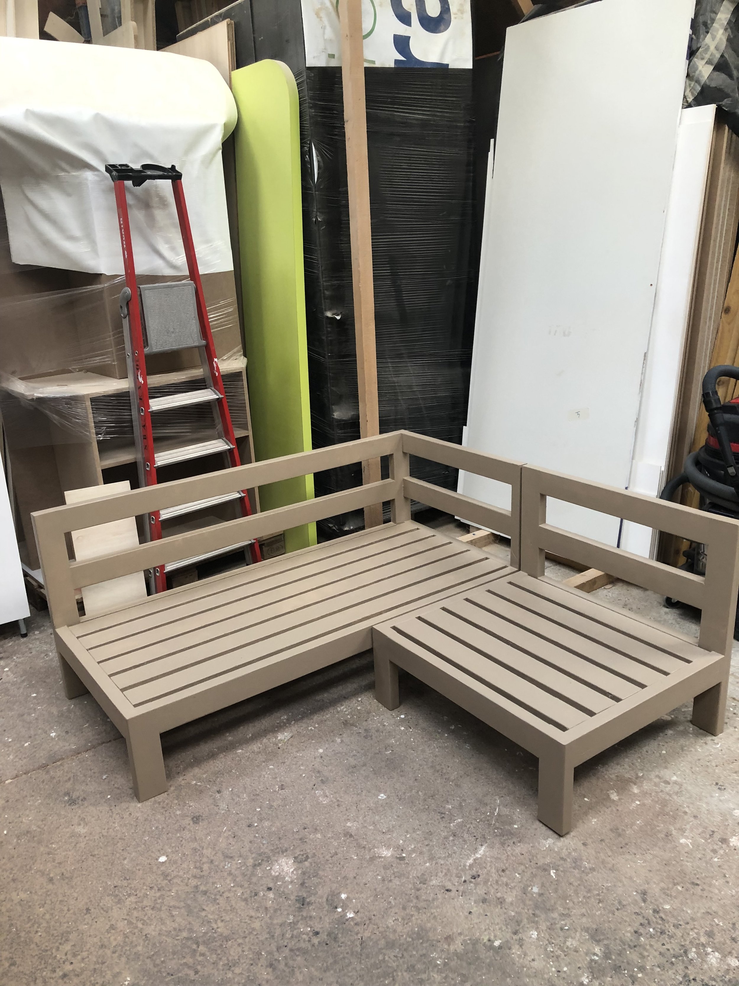 Un cadre en bois avec un banc en plastique gris clair, en cours d'assemblage, dans un atelier avec divers matériaux et outils. 