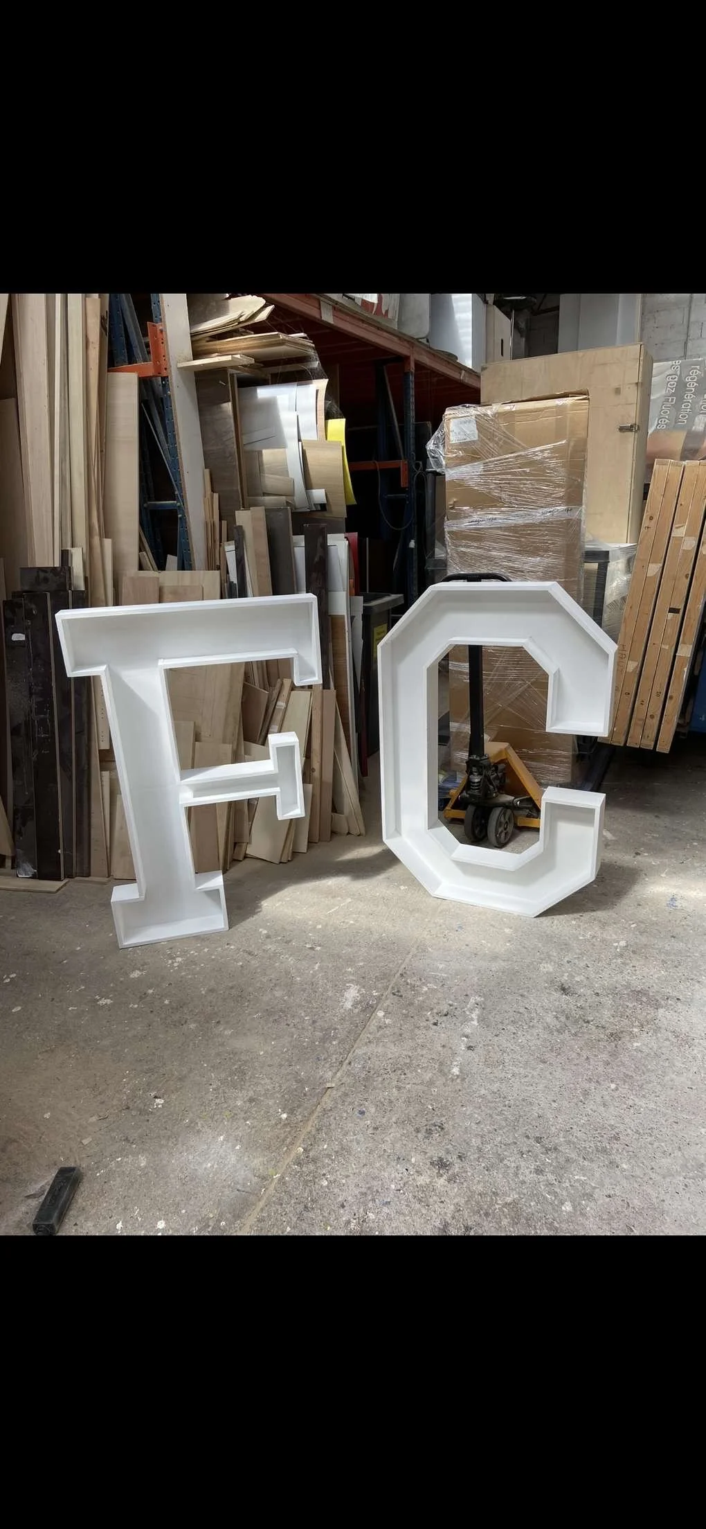 Lettres en relief en forme de 'F' et 'C' en blanc dans un atelier de menuiserie.