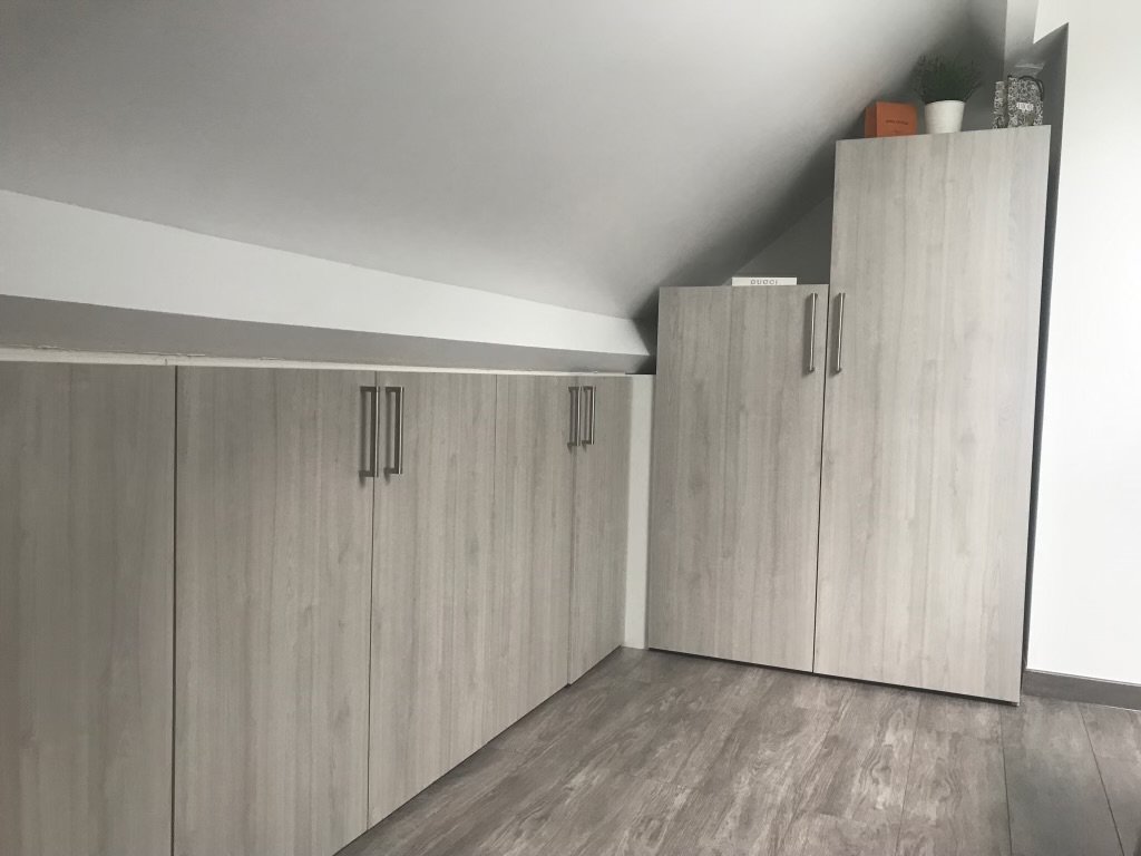 Armoires en bois clair dans un coin de pièce sous un plafond en pente.