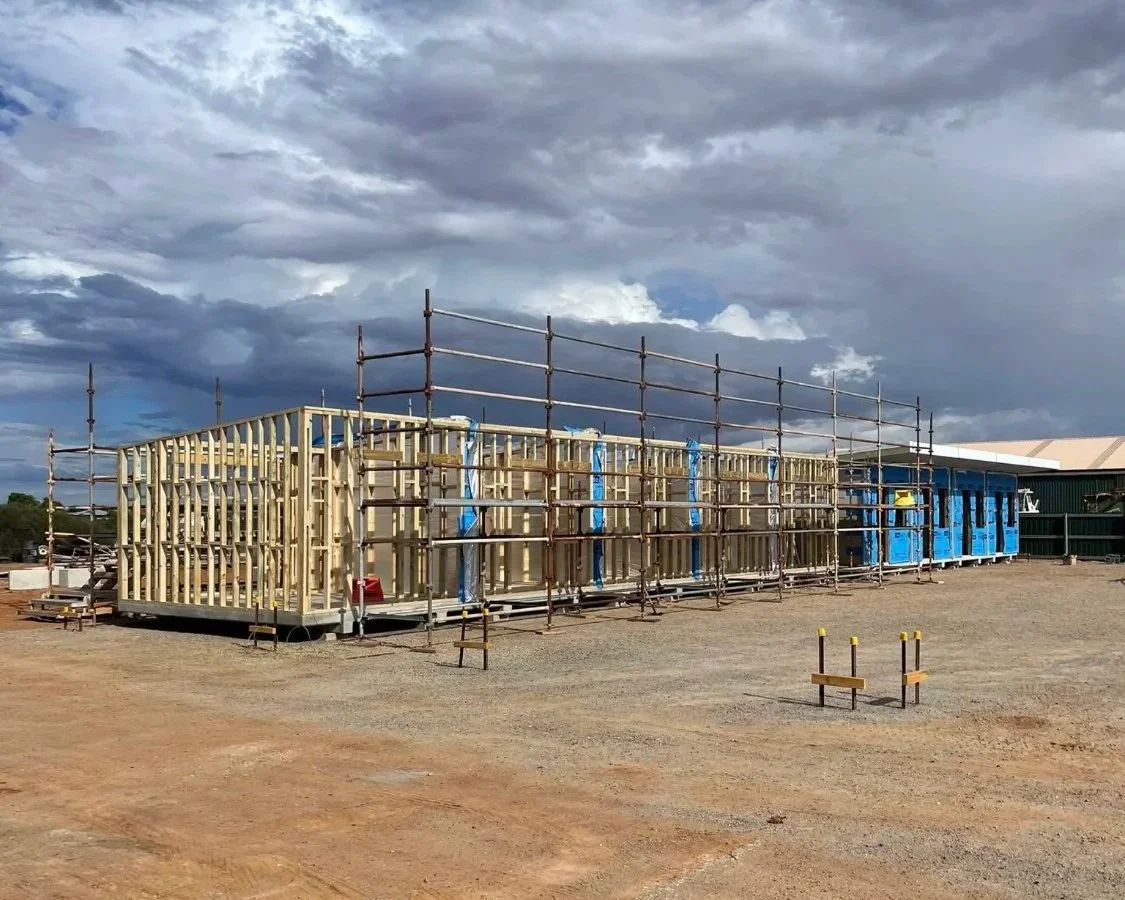 Construction site with wooden frame and scaffolding for a building, under a cloudy sky.