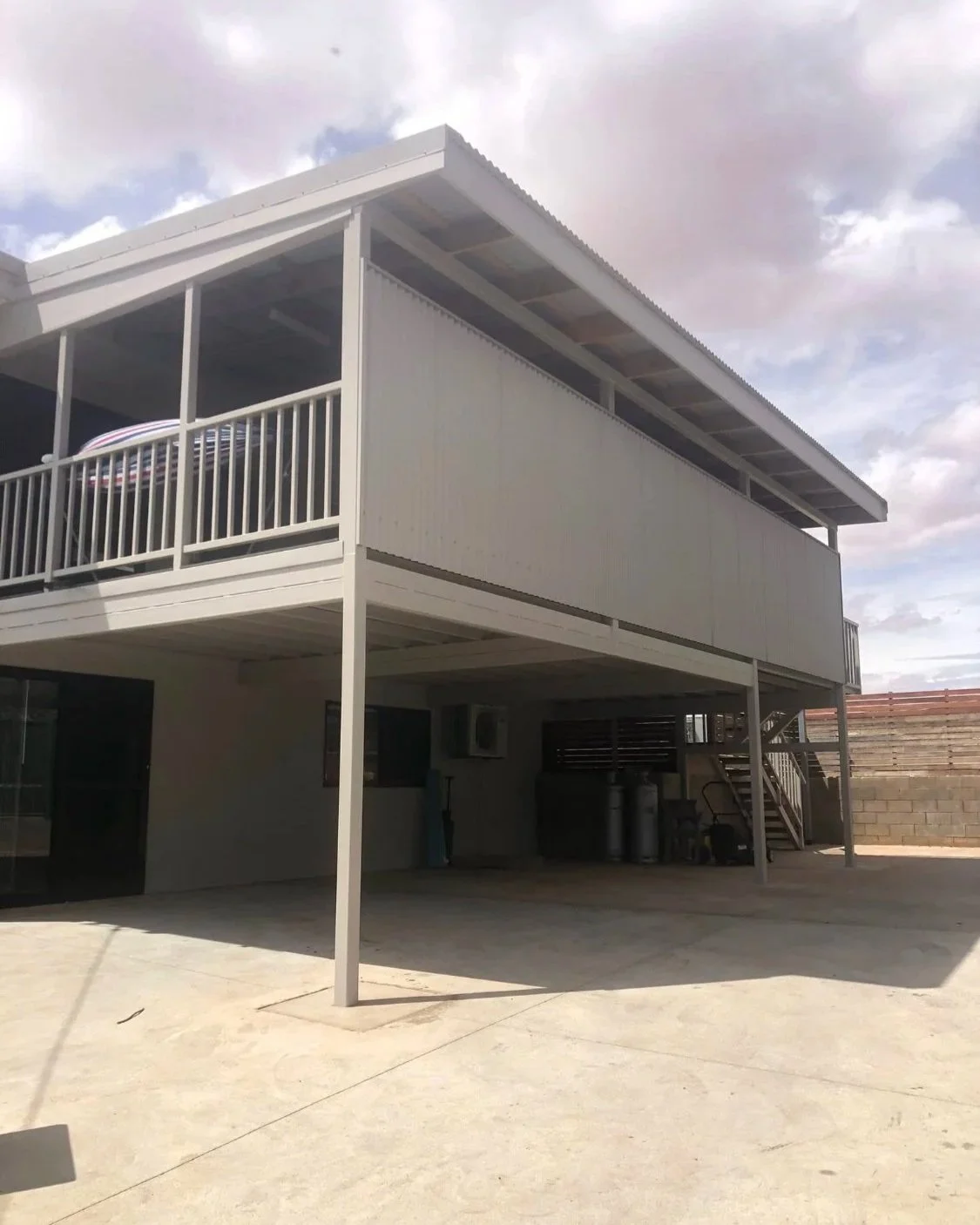 Two-story house with a white balcony on the second floor, concrete driveway, and a partly cloudy sky.