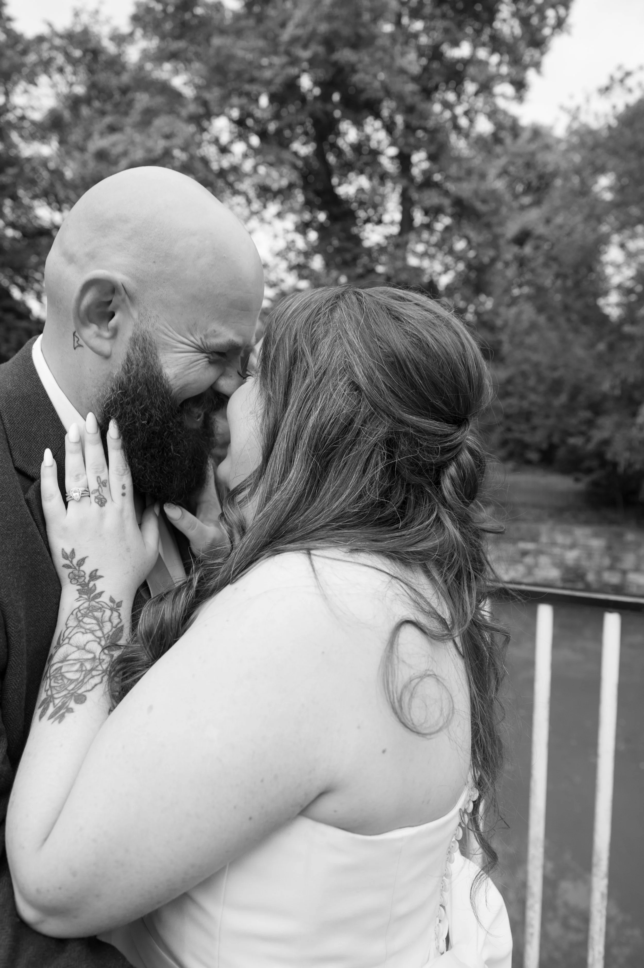 A black and white photo of a couple sharing an intimate moment outdoors, with the man smiling and the woman gently touching his face.