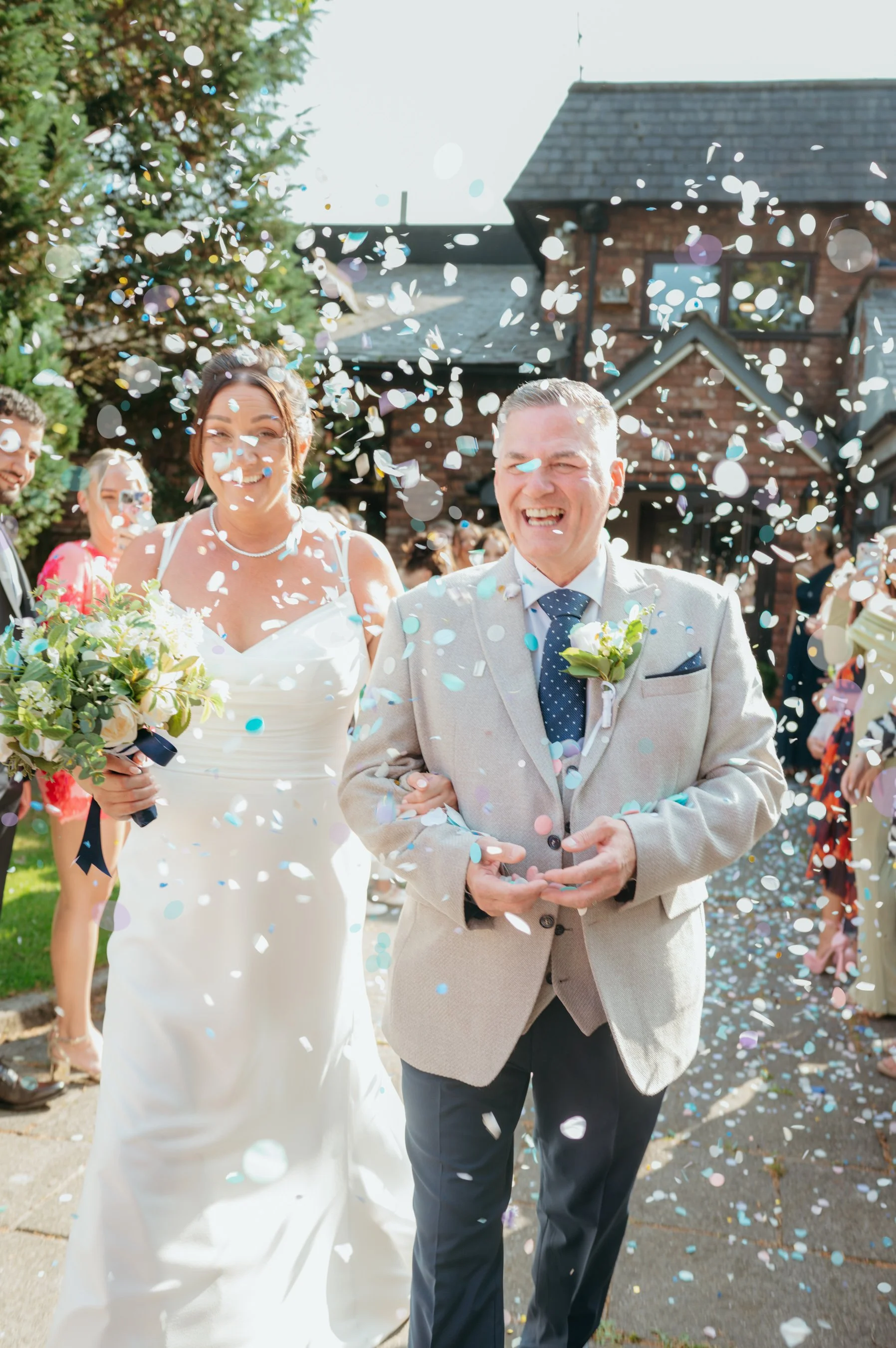 A bride and groom exit a wedding ceremony surrounded by colorful confetti and happy guests.